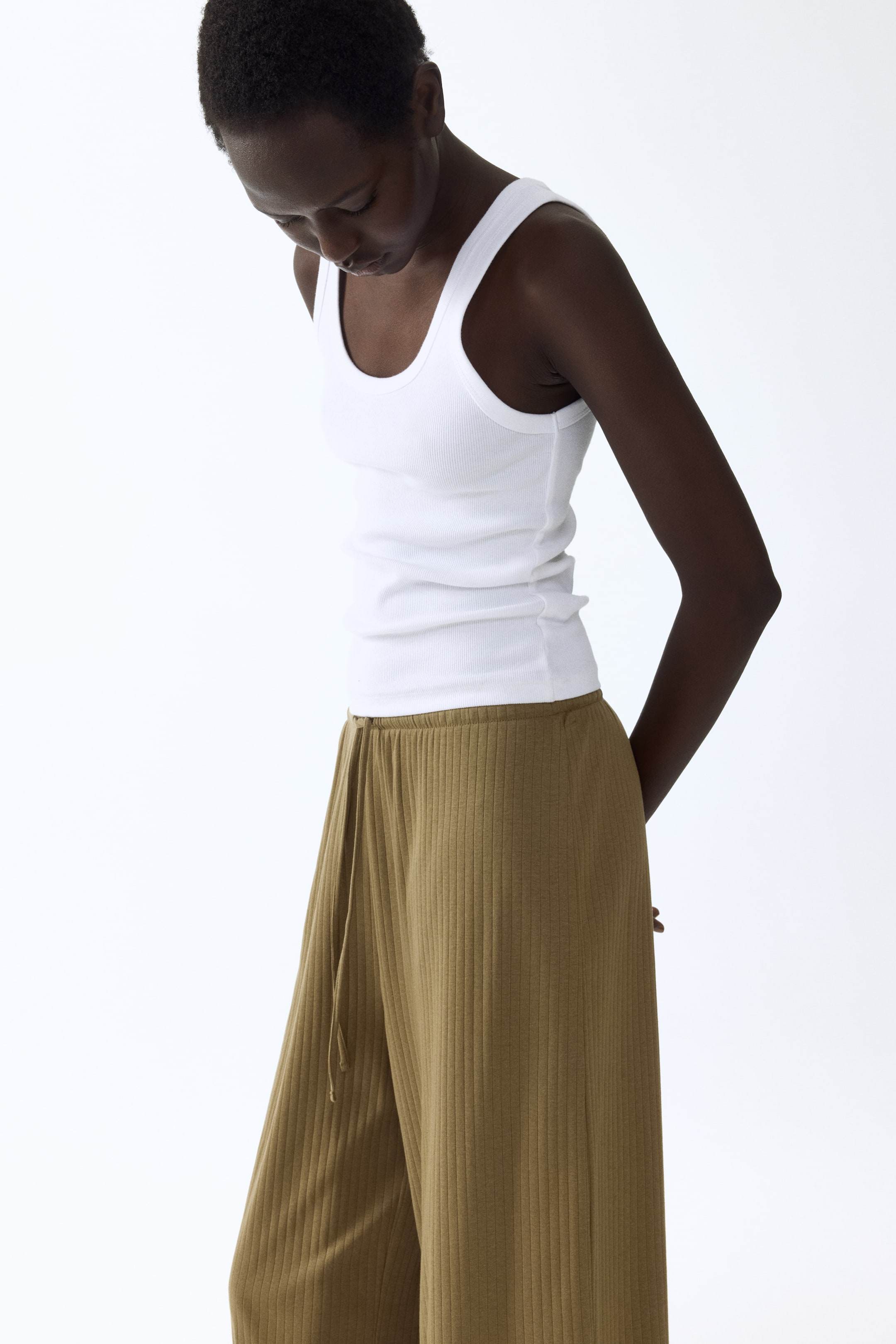 View larger image: "Sporting a white ribbed scoop neck tank top paired with olive green ribbed wide-leg pants, which showcase a visible drawstring waist and offer a relaxed fit."