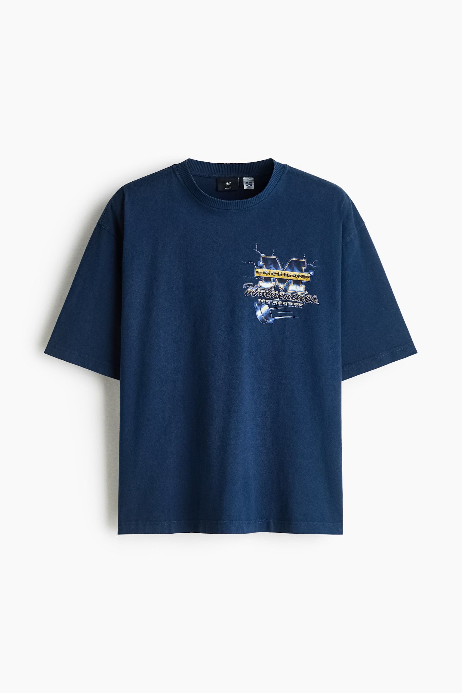 Egy sÃ¶tÃ©tkÃ©k, nehÃ©z pamut jersey pÃ³lÃ³ elÃ¶lnÃ©zetben lÃ³g, laza fazonnal, bordÃ¡zott kerek nyakkivÃ¡gÃ¡ssal, ejtett vÃ¡llakkal Ã©s egyenes alsÃ³ szegÃ©llyel. A pÃ³lÃ³ bal mellrÃ©szÃ©n a âMichigan Wolverines Ice Hockeyâ grafikai nyomat lÃ¡thatÃ³.