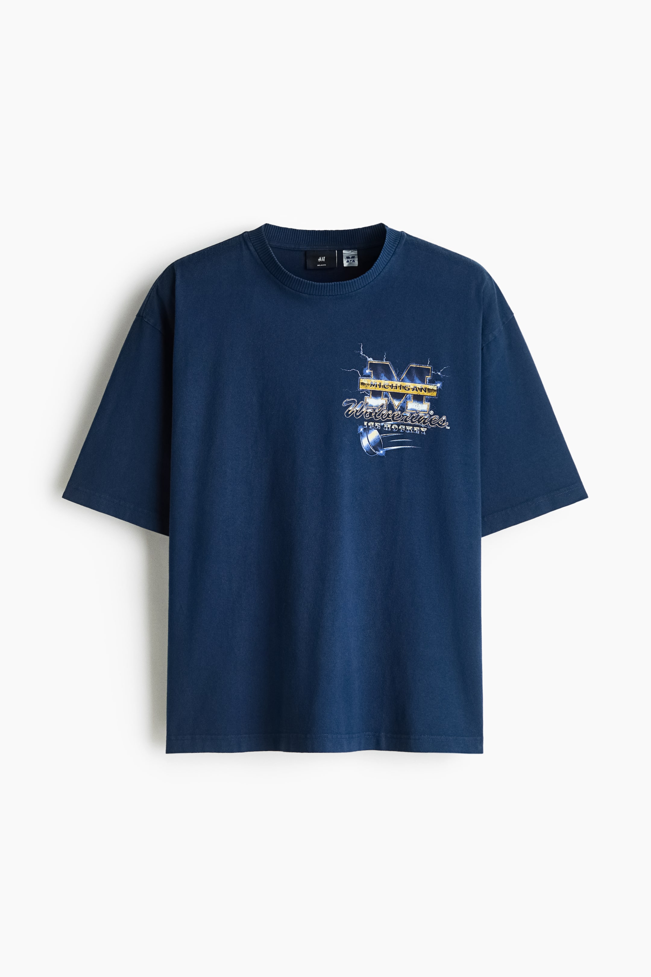 Größeres Bild ansehen: Ein marineblaues, schweres Baumwolljersey-T-Shirt hängt in frontaler Ansicht und bietet eine lockere Passform mit geripptem Rundhalsausschnitt, überschnittenen Schultern und geradem Saum. Auf der linken Brust zeigt das T-Shirt einen grafischen Print mit „Michigan Wolverines Ice Hockey“.