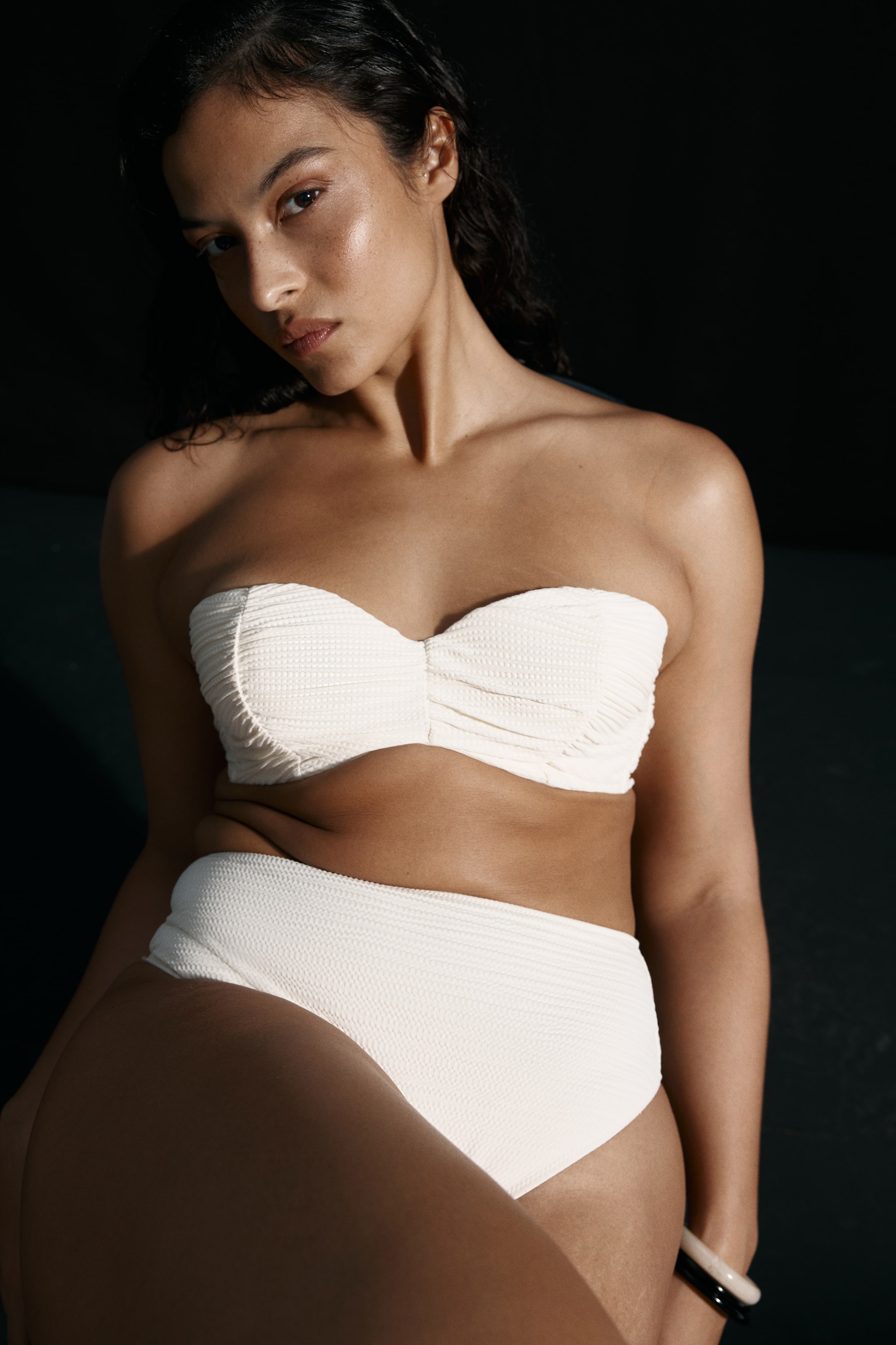 Ver imagen más grande: La modelo lleva braguitas de bikini de talle alto en un tejido texturizado color crema, combinadas con un top de bikini sin tirantes a juego.