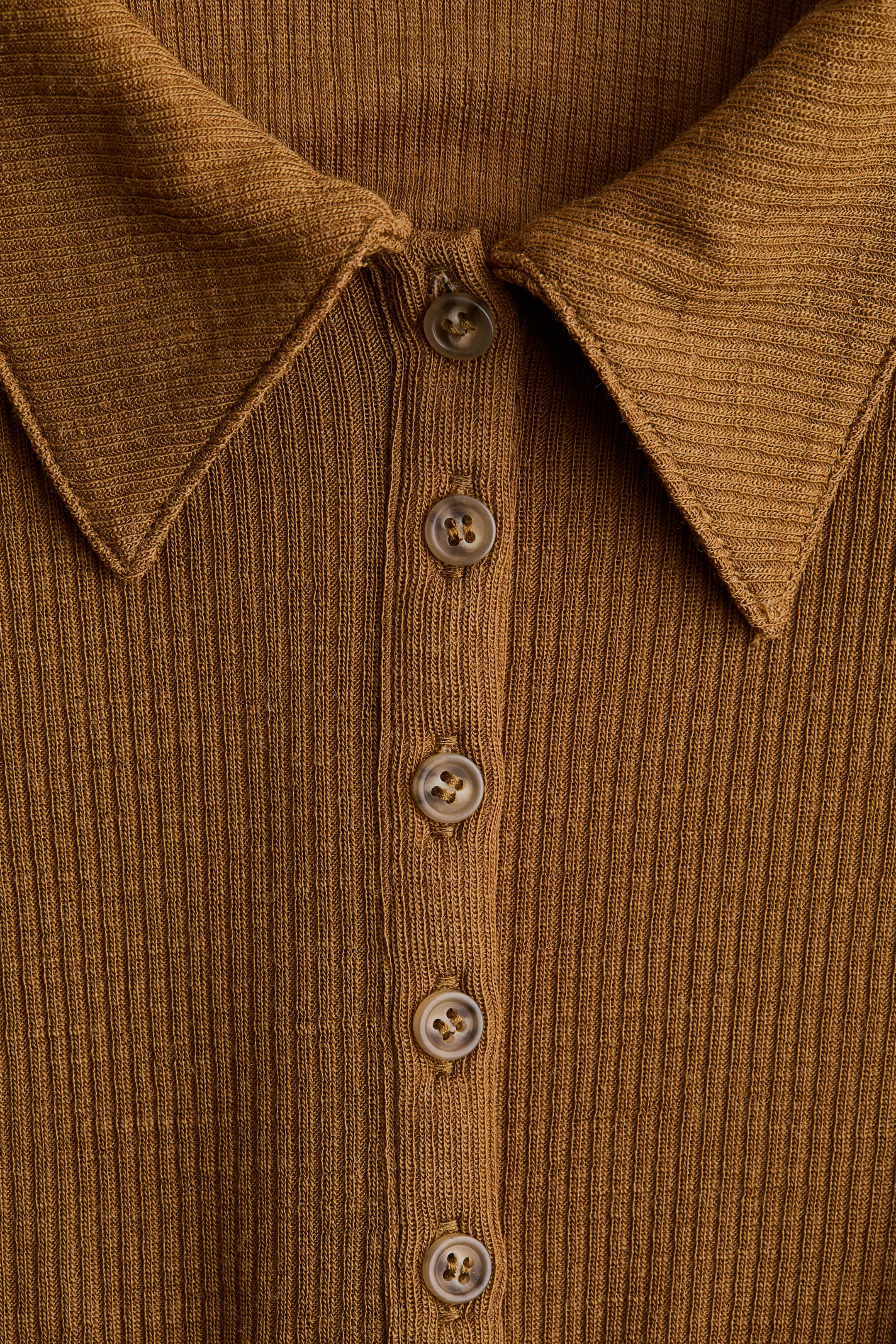 Ampliar la imagen: Un top de punto acanalado en color marrón presenta un cuello en punta y una tapeta delantera con botones, que está asegurada por cinco botones circulares de color marrón marmoleado.