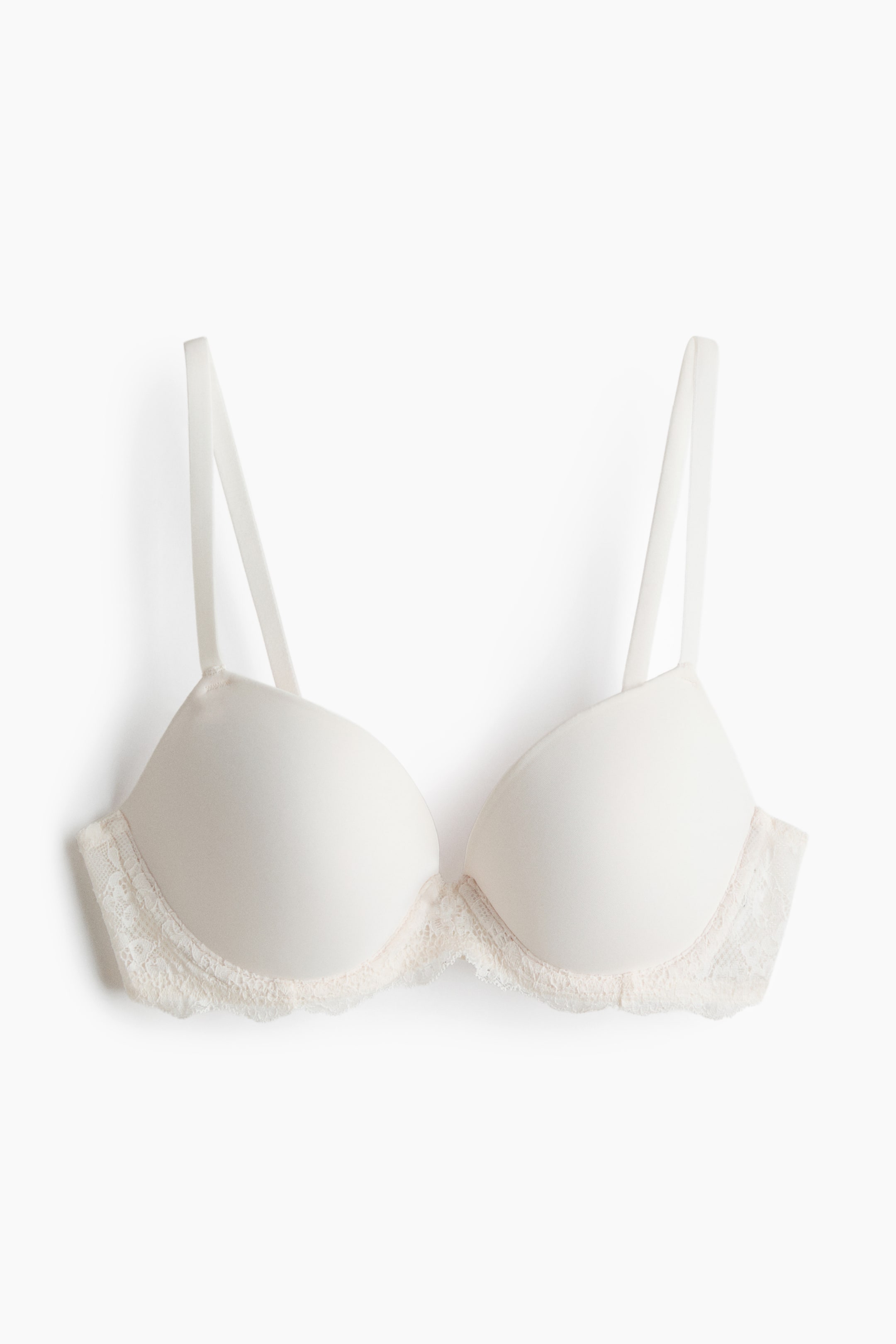View larger image: The image displays a push-up bra from the front, showcasing smooth, molded cups in an off-white hue. The lower edges of the cups are adorned with delicate lace trim, while thin, adjustable shoulder straps extend upwards.