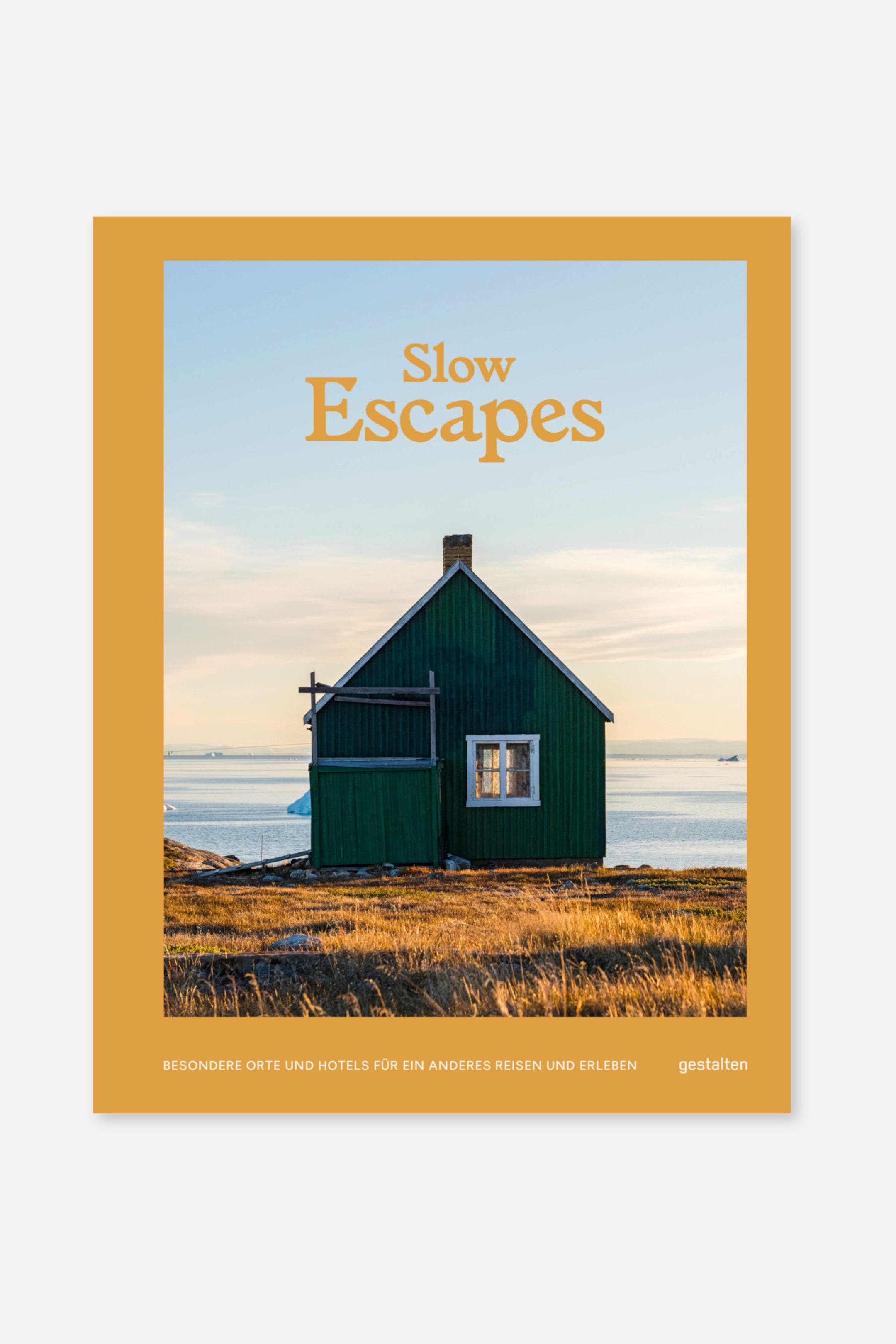 Größeres Bild anzeigen: Ein frontales Buchcover zeigt einen dicken senfgelben Rand um ein Bild eines grünen Holzhauses an einer felsigen Küste neben Wasser und Himmel, mit dem orangefarbenen Titel "Slow Escapes" oben. Kleinere weiße Schrift am unteren Rand liest "BESONDERE ORTE UND HOTELS FÜR EIN ANDERES REISEN UND ERLEBEN" und "gestalten".