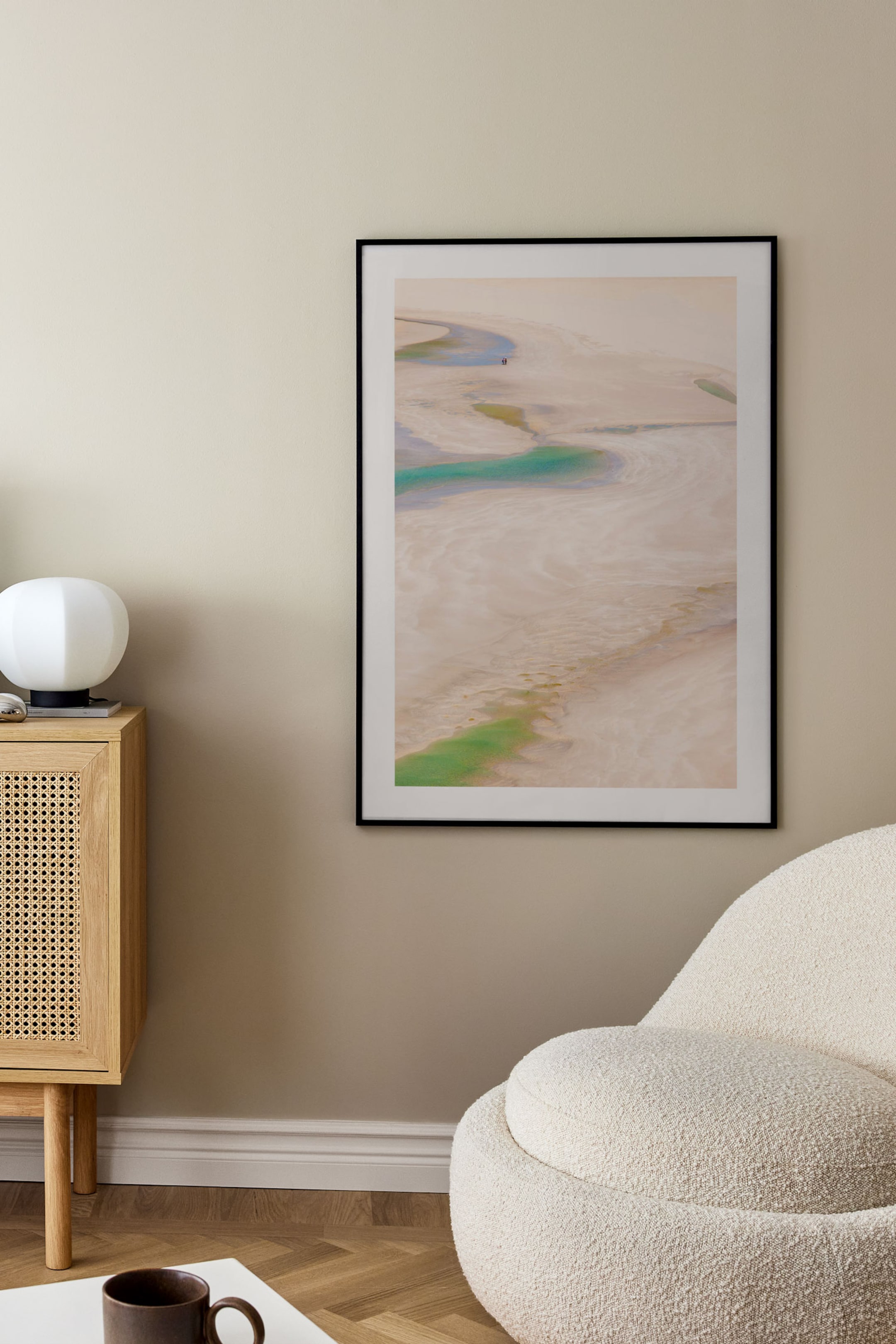 Grotere afbeelding bekijken: Een kunstdruk toont een abstract landschap vanuit vogelperspectief, met lichte beige en zandtinten en kronkelige gebieden van levendig groen en turquoise kleuren. Het is gepresenteerd in een dunne zwarte lijst met een witte rand.