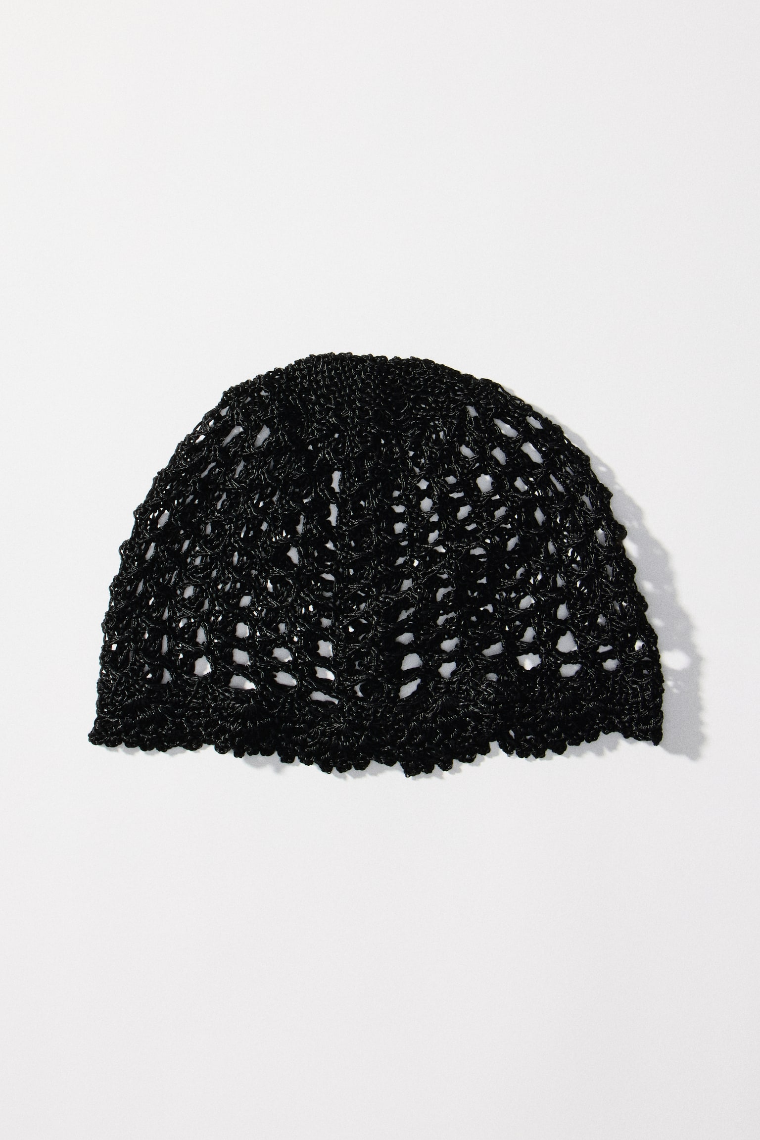 A black crocheted cap showcases a wide mesh pattern and features a decorative, scalloped border along its lower edge. - 1