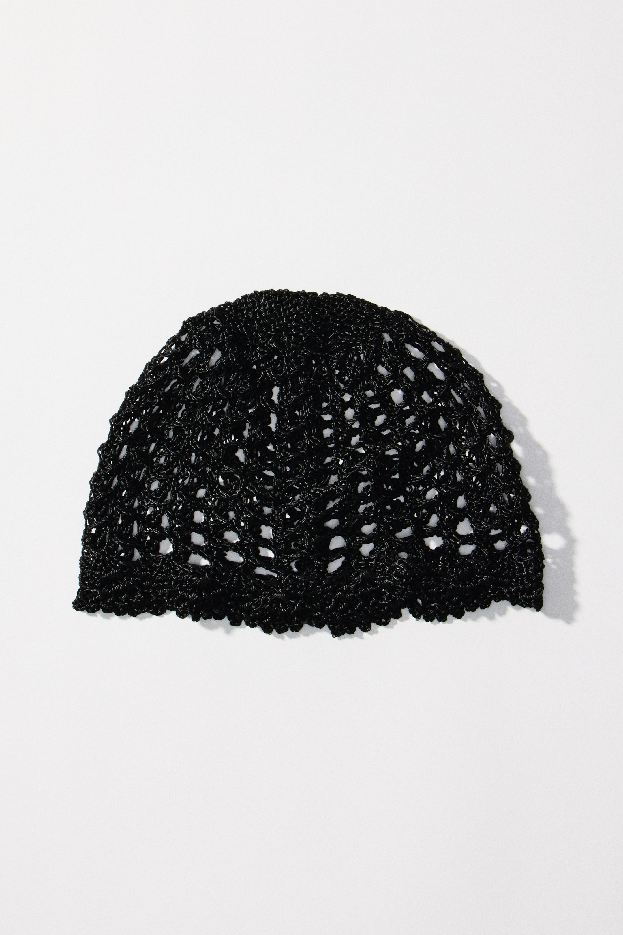 View larger image: A black hat showcases a shimmering, crochet-look viscose knit. The hat is completed with a scalloped trim along its bottom edge.