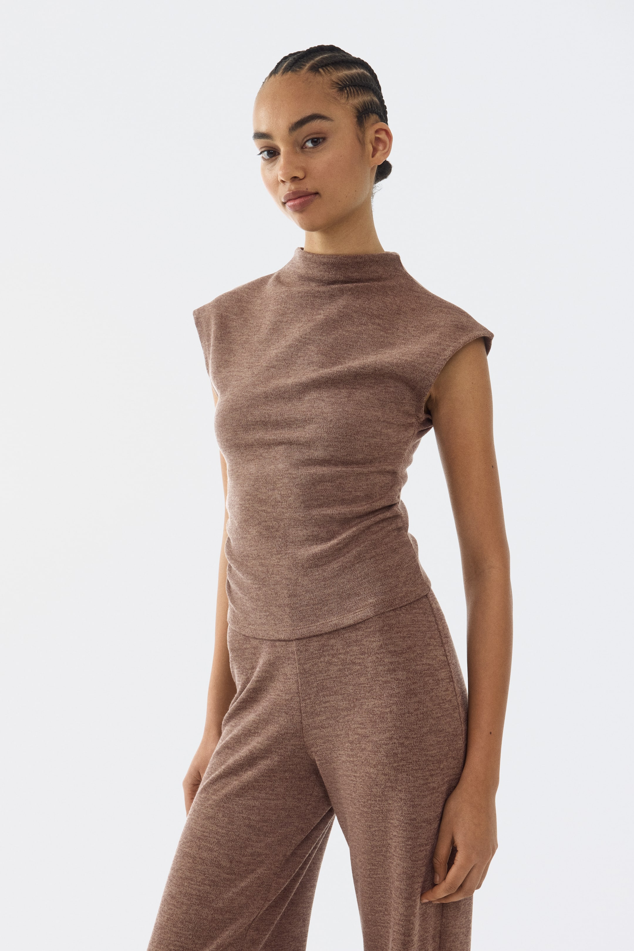 Ver imagem maior: Uma camisola de malha castanha mesclada com gola alta simulada e ombros prolongados está a ser usada com calças largas a condizer, apresentando um conjunto coordenado de um ligeiro ângulo frontal direito.