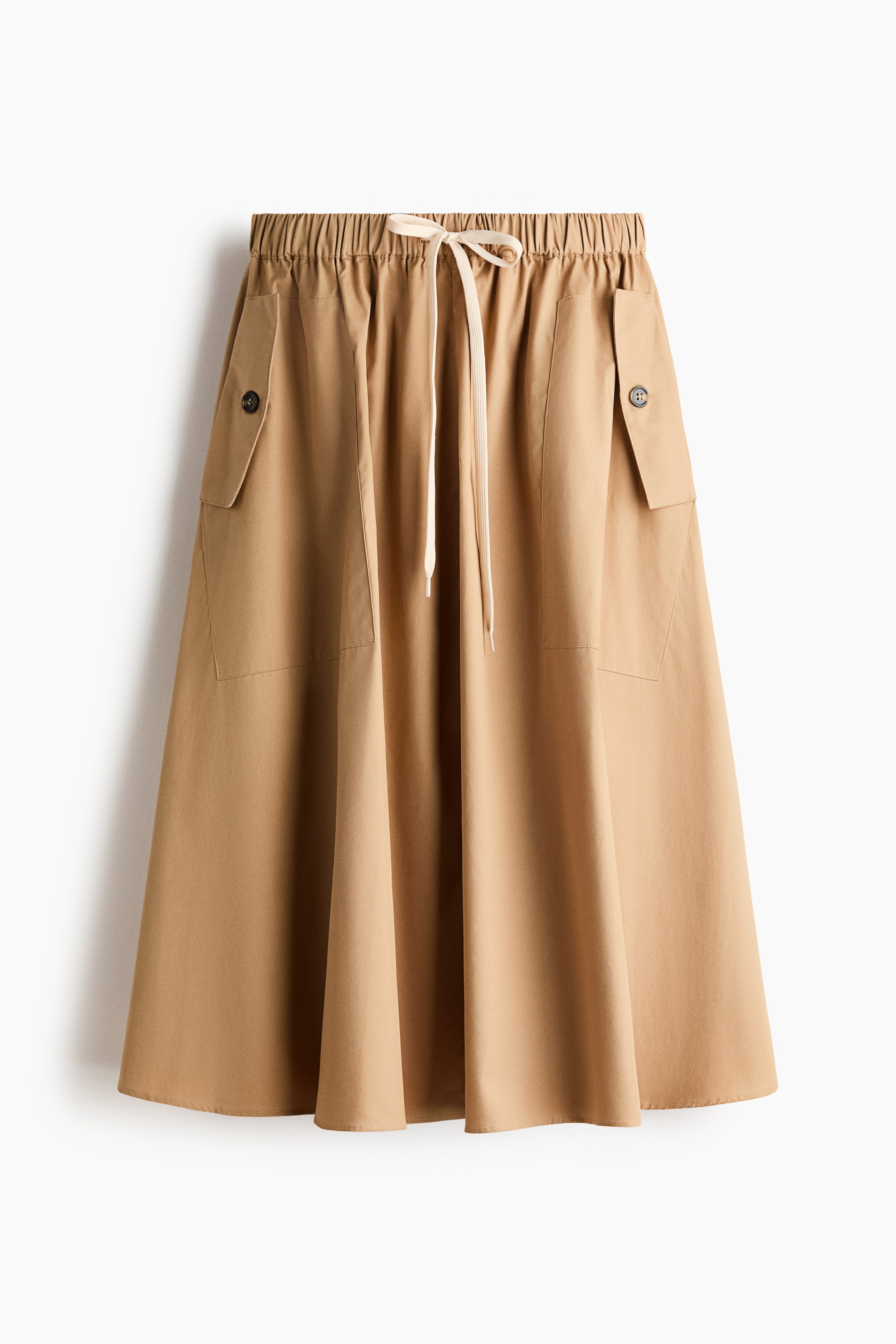 View larger image: Presenting a tan A-line skirt from the front, this piece features an elasticated waistband with a cream drawstring tie. It includes two large patch pockets, each adorned with a flap and a single dark button, gracefully flowing to a midi length.