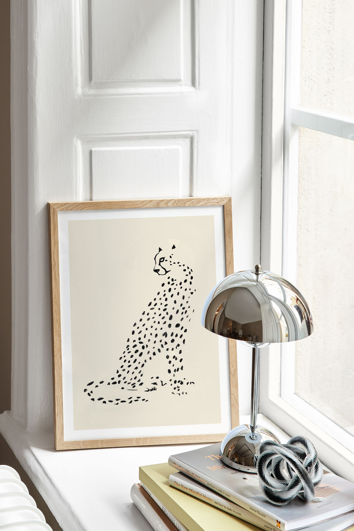 Una stampa dâarte presenta unâillustrazione minimalista a inchiostro nero di un ghepardo seduto che si volta a guardare oltre la spalla, su uno sfondo color crema chiaro. La forma del ghepardo Ã¨ resa con semplici macchie nere e contorni, e la stampa Ã¨ rifinita con un bordo bianco.