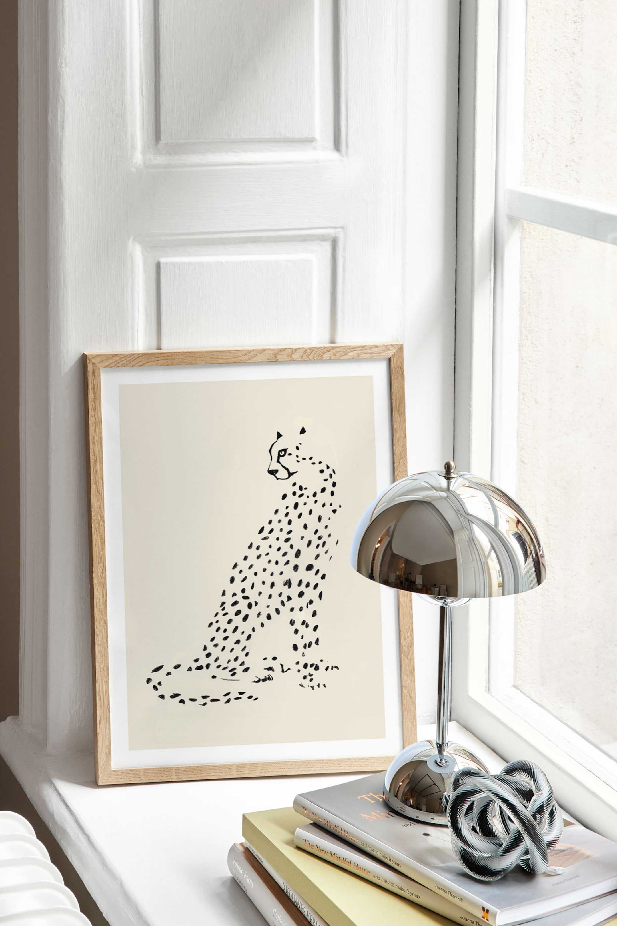Visualizza immagine più grande: Una stampa d’arte incorniciata mette in risalto un’illustrazione minimalista in bianco e nero di un ghepardo seduto di profilo su uno sfondo beige chiaro. L’opera è inserita in una cornice in legno naturale chiaro con un’ampia passpartout bianca, con il ghepardo illustrato rivolto verso sinistra.