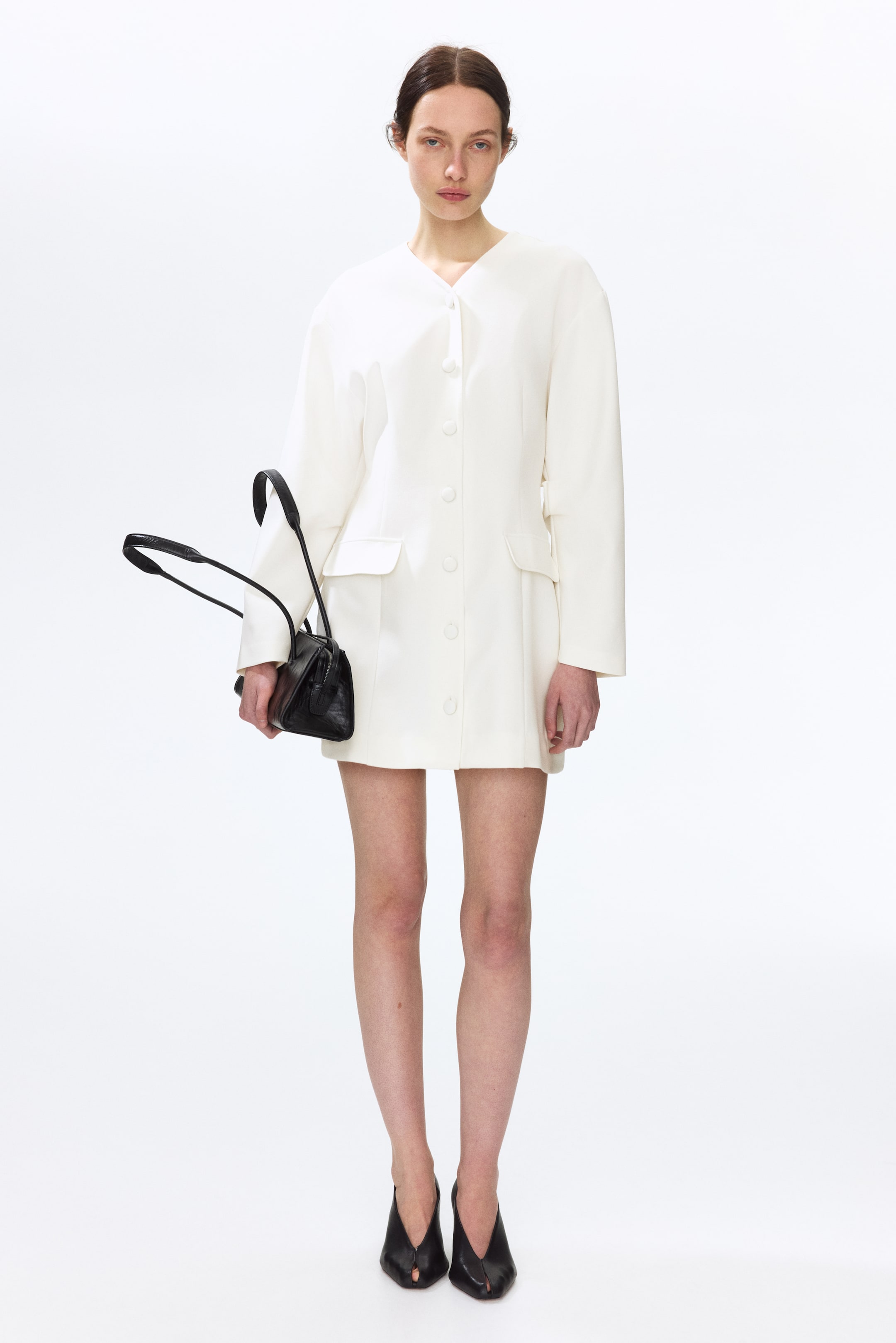 Ampliar la imagen: Un vestido blanco roto presenta un escote en V sin cuello y un cierre frontal con botones redondos. Muestra mangas largas y sueltas, una silueta de hombros anchos y dos bolsillos de parche rectangulares en el frente, llegando hasta la mitad del muslo.