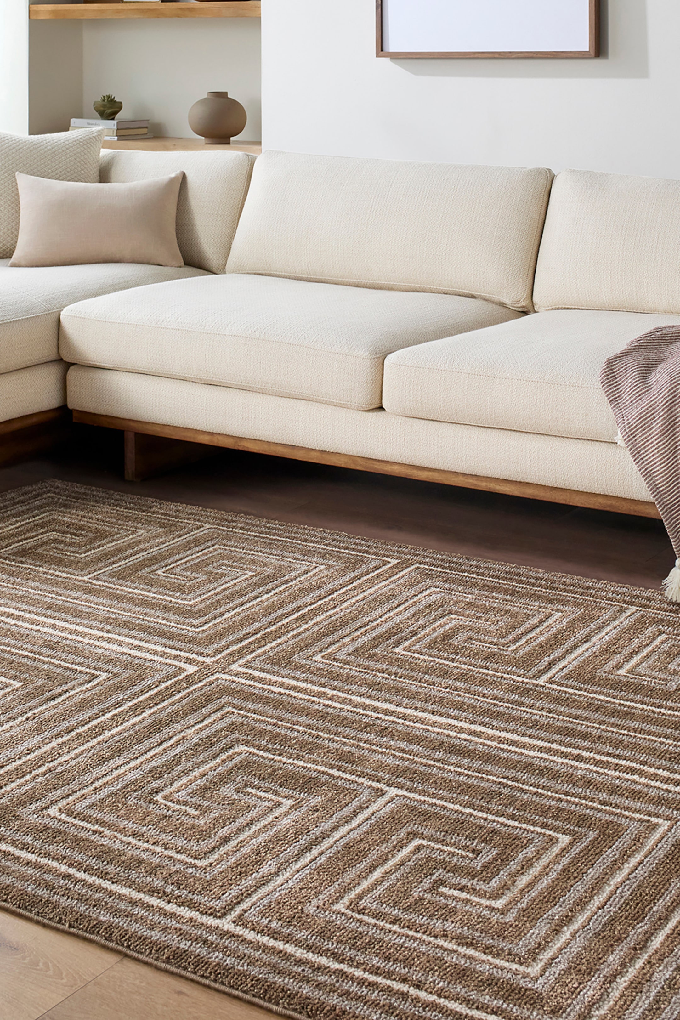 View larger image: A rectangular area rug features a repeating geometric Greek key pattern made up of interlocking concentric square spirals. The low-pile, textured woven rug uses a neutral colour palette of brown, beige, and cream stripes that highlight the structured design.