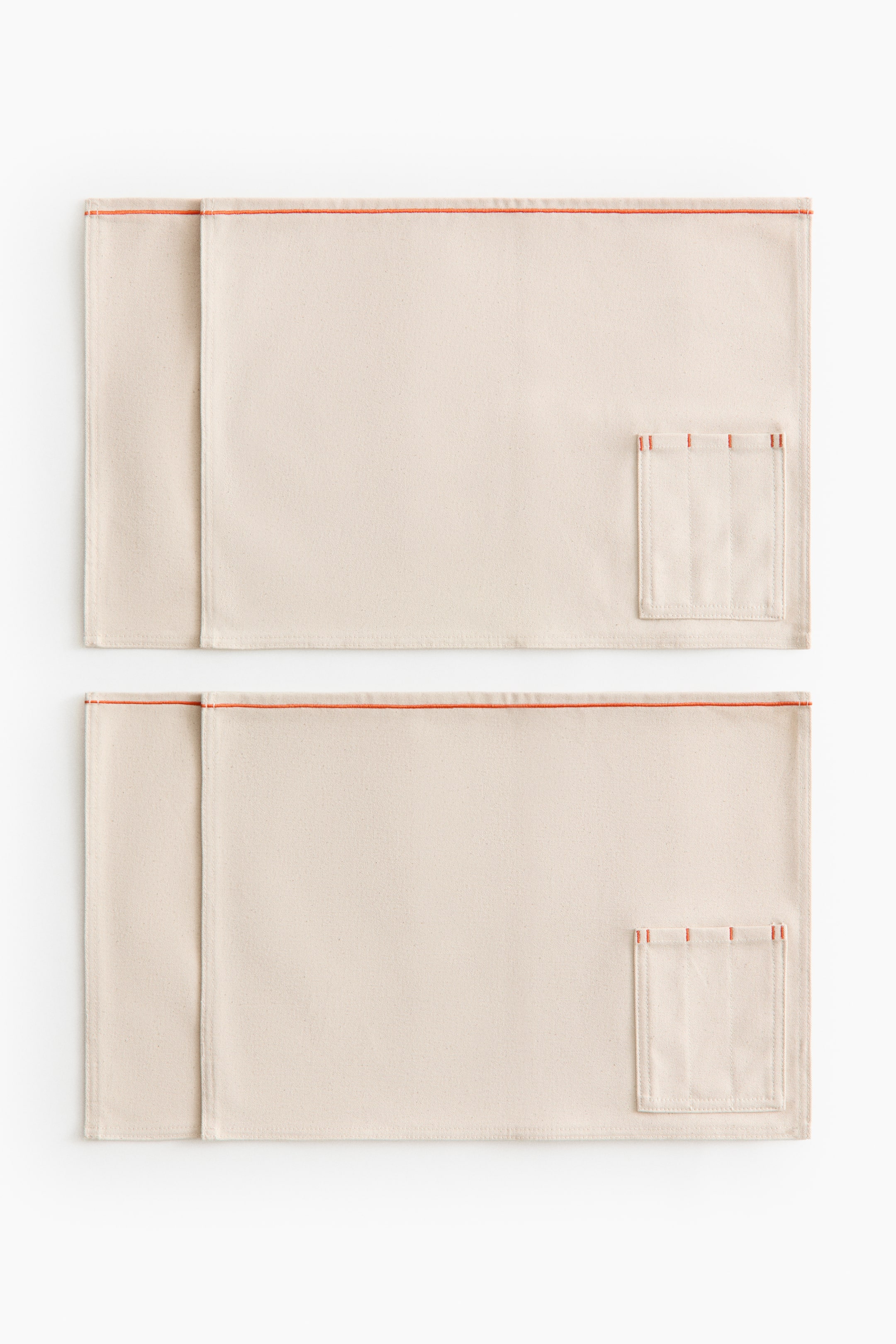 View larger image: Two rectangular, light beige fabric mats are laid flat, each showcasing a horizontal orange-red stripe along the top edge. Each mat displays a vertical fold along its left side and a small patch pocket on the right, detailed with three orange-red bar-tack stitches at the top.