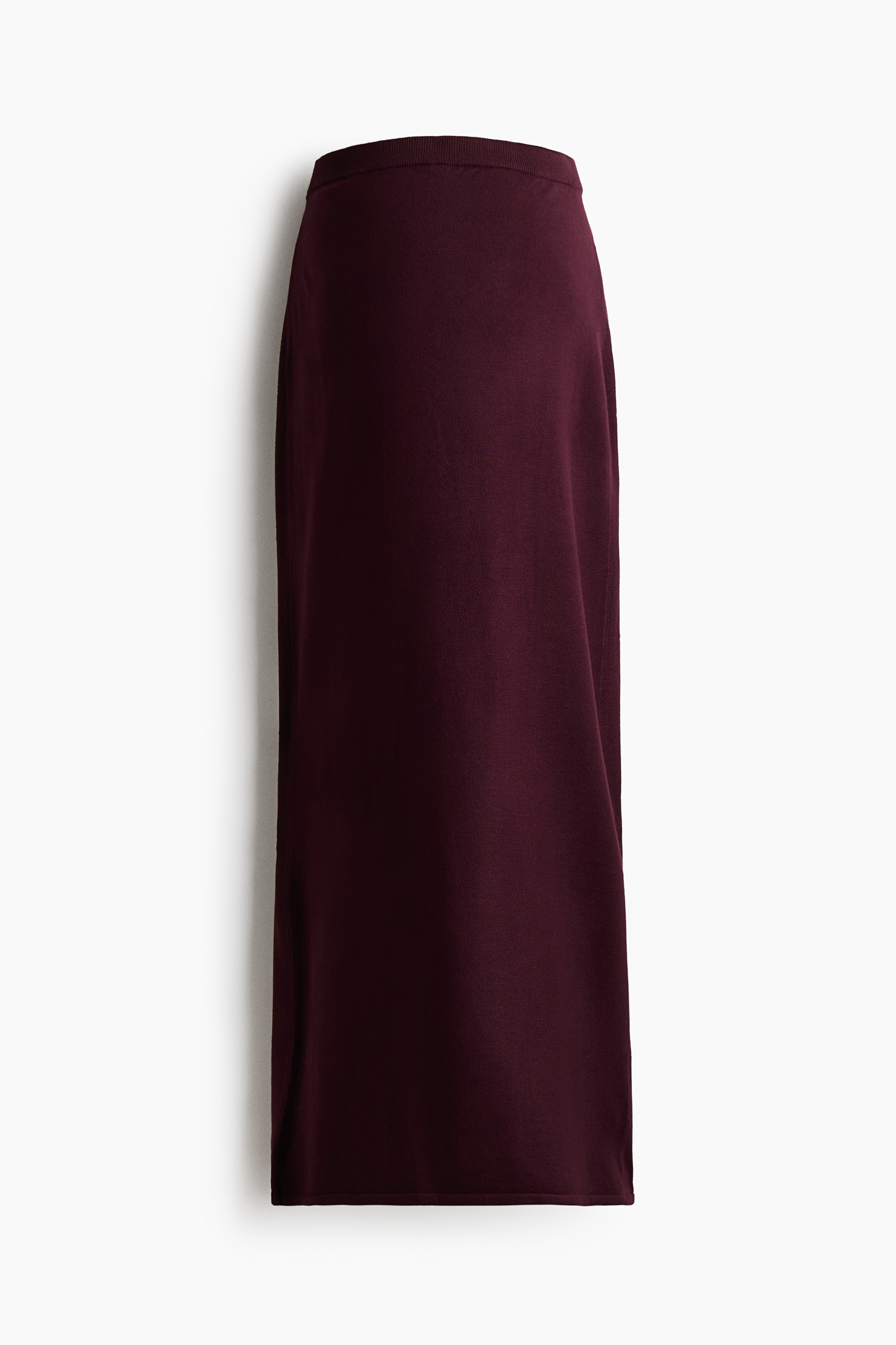 A modell egy bokaig érÅ, testhez simuló kötött szoknyát visel mély bordó szÃnben, amelyet sötét, texturált kötött pulóverrel és fekete slingback lapos cipÅkkel párosÃtottak. A szoknya egyenes szabásvonalú, finom kötött textúrával.