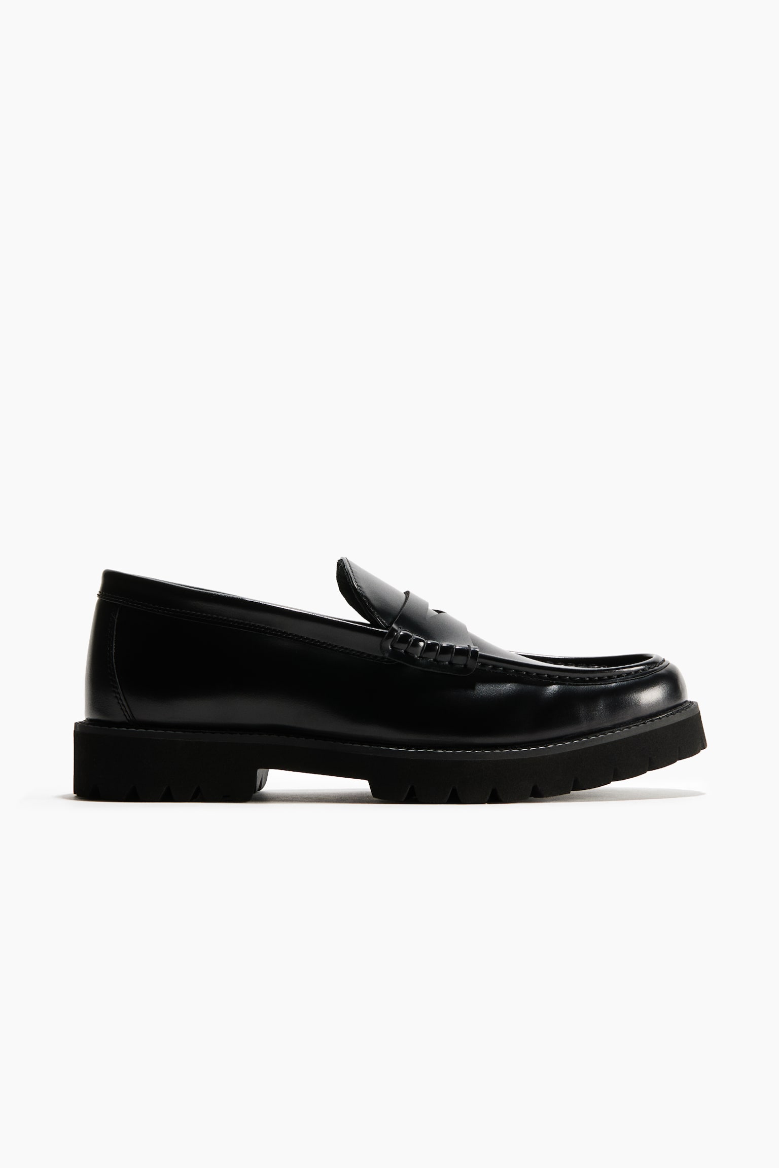 A black leather penny loafer is shown in a side-profile view, featuring a polished leather upper with a classic strap across the vamp and moc-toe stitching. The shoe is constructed with a thick, lugged black rubber sole that gives it a rugged silhouette.