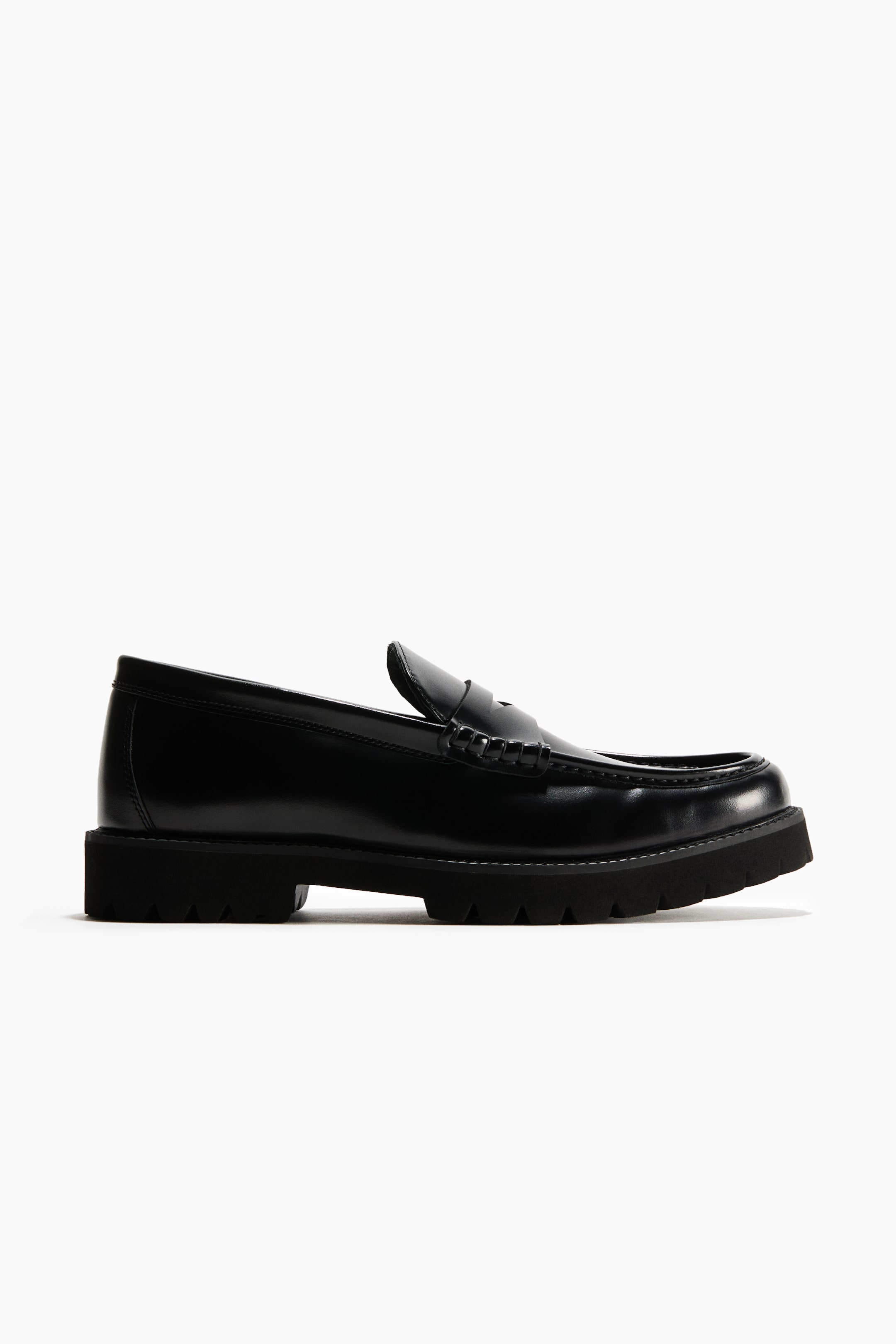 View larger image: A black leather penny loafer is shown in a side-profile view, featuring a polished leather upper with a classic strap across the vamp and moc-toe stitching. The shoe is constructed with a thick, lugged black rubber sole that gives it a rugged silhouette.