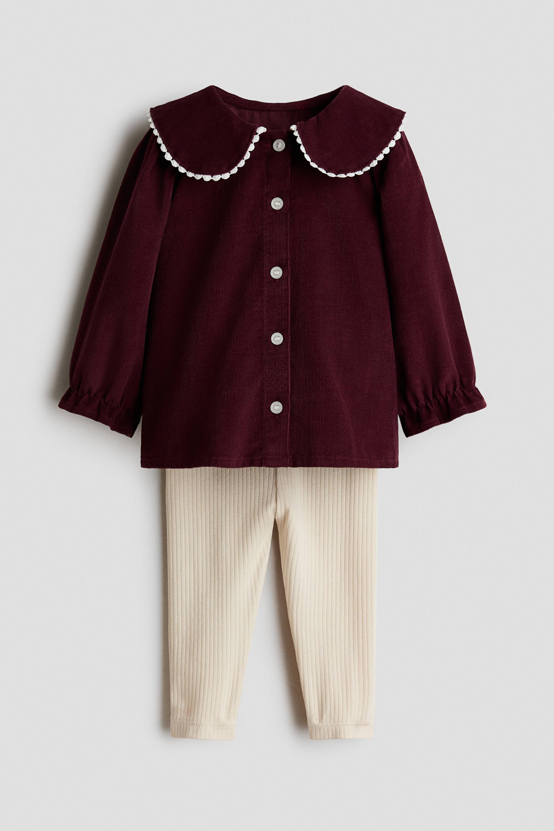 View larger image: A two-piece outfit features a dark red corduroy top with a rounded Peter Pan collar accented by a white scalloped trim, white buttons down the front, and elasticised cuffs on the long sleeves. Cream-coloured ribbed knit pants appear beneath the top.