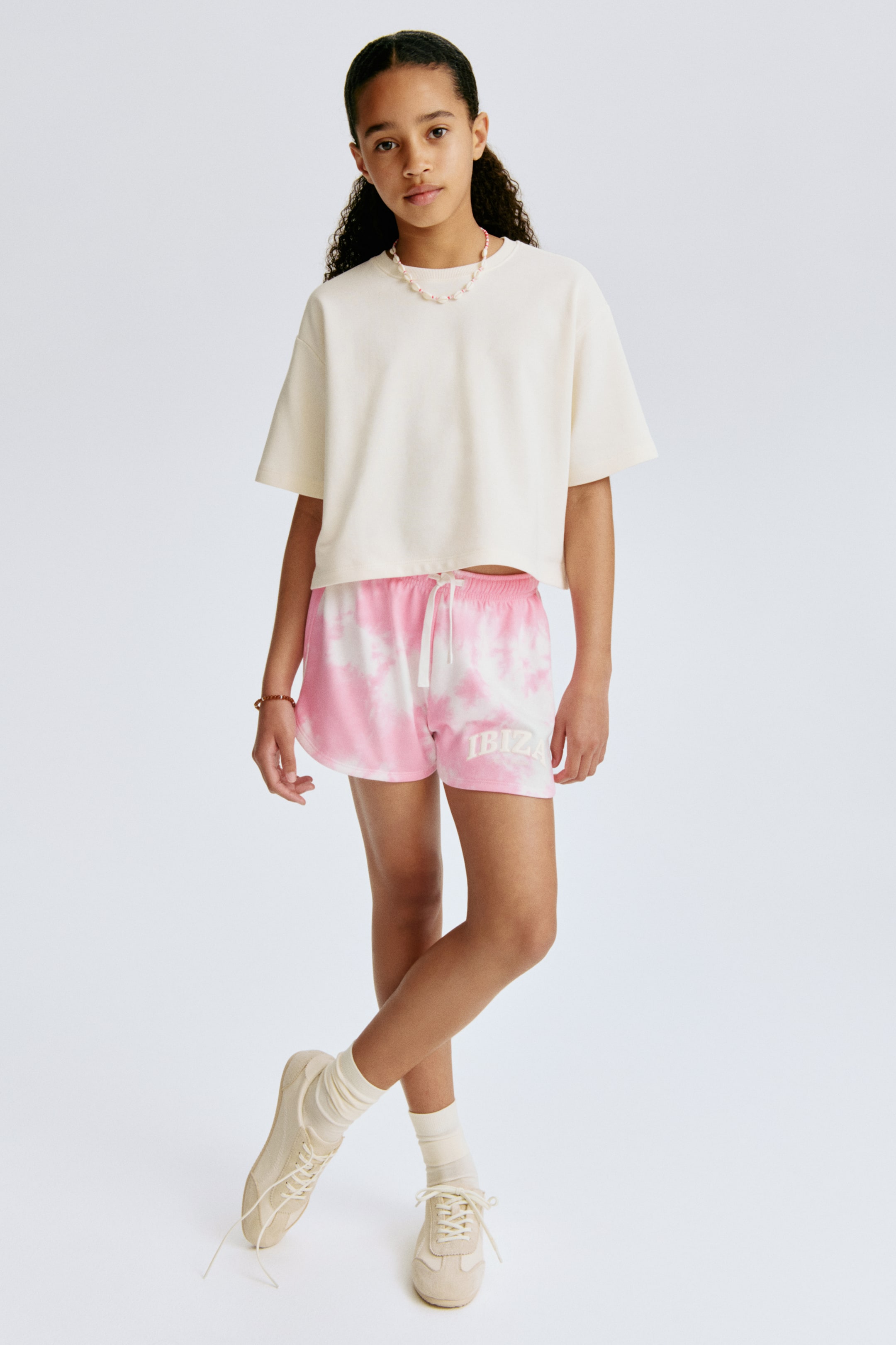 View larger image: The shorts are facing forward, showcasing a pink and white tie-dye pattern, with an elastic waistband and a visible white drawstring tied at the front. "IBIZA" is printed in white on the left leg. They feature a curved hem on both legs, offering a relaxed fit.
