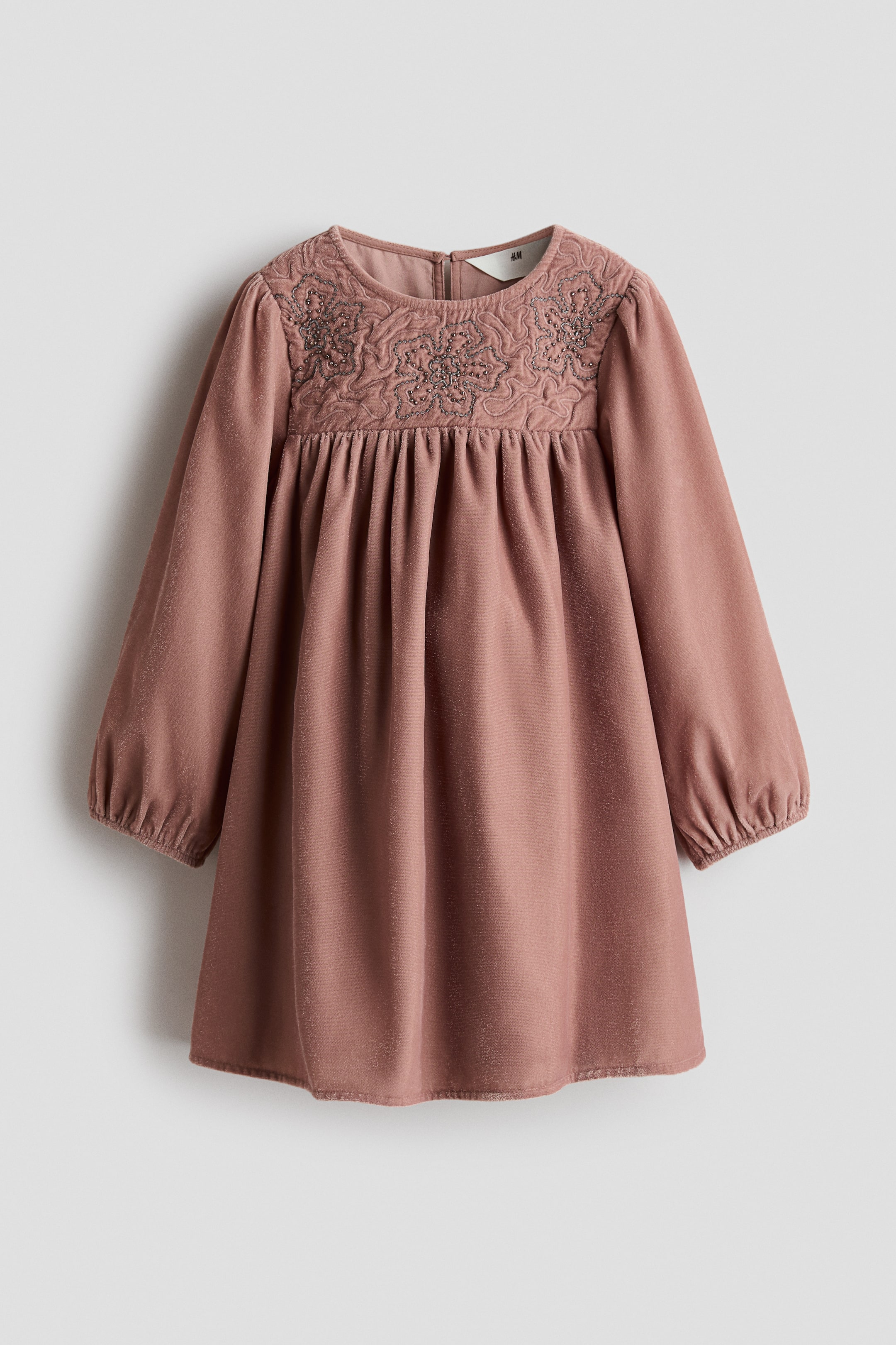 View larger image: A dusty pink long-sleeved dress is facing front, featuring a round neckline and a high-waisted yoke with beaded floral embroidery. The fabric is gathering below the yoke to create a flared skirt, and the long sleeves are ending in elasticated cuffs.