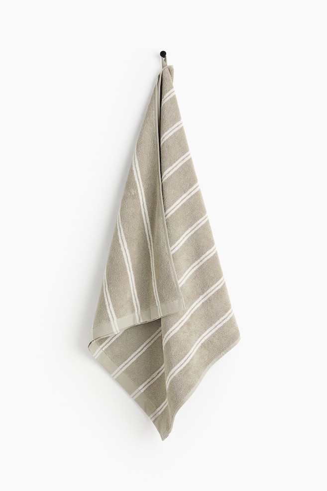 A taupe terry towel is showcasing its front, featuring horizontal white stripes of varying widths. The towel is folded over at the top, forming a draped, triangular shape. - 1