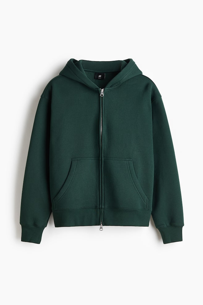 A dark green zip-up hoodie is shown facing front, featuring a silver-tone two-way zipper, dropped shoulders, and a split kangaroo pocket. The hoodie is displaying ribbed cuffs on the long sleeves and a matching ribbed hem. - 1