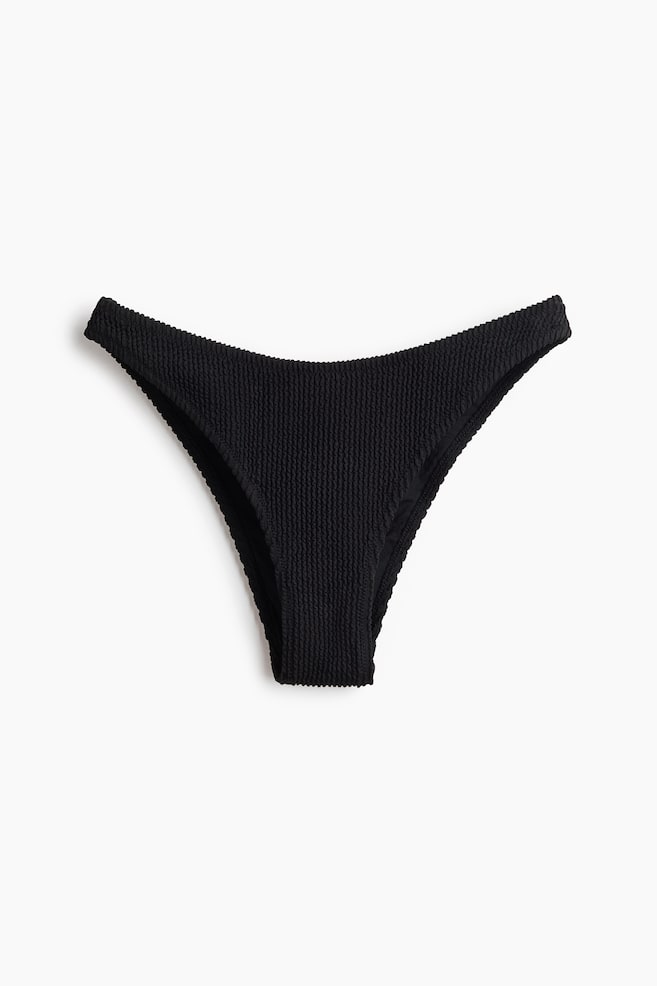Braguitas de bikini negras con textura se muestran desde el frente, con una cintura baja y curvada y aberturas de pierna de corte alto. - 1
