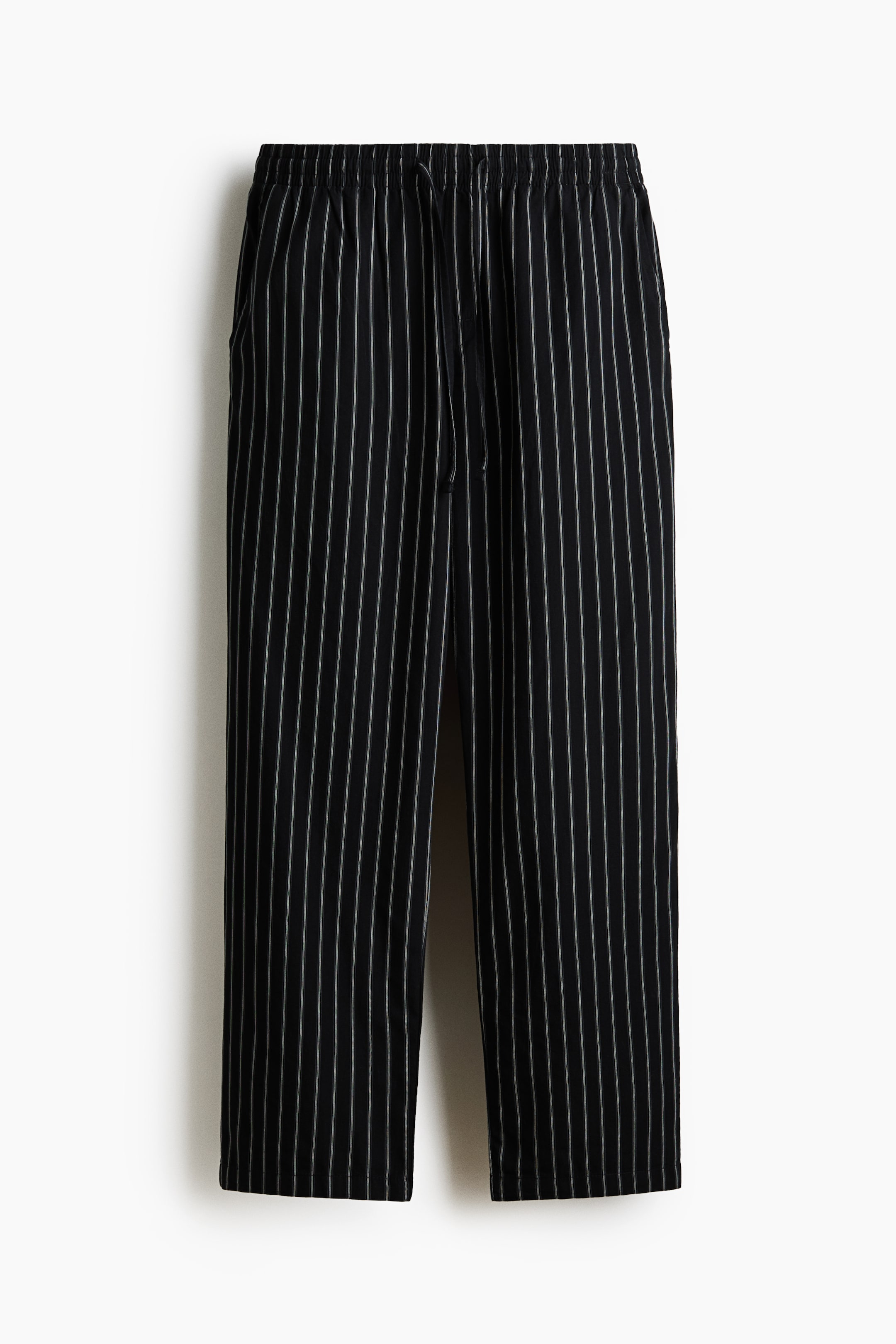 Ver imagen más grande: Pantalones negros con finas rayas verticales blancas colgados en plano, vistos de frente. Presentan cintura elástica con cordón visible y bolsillos laterales, mostrando un corte recto de pernera.