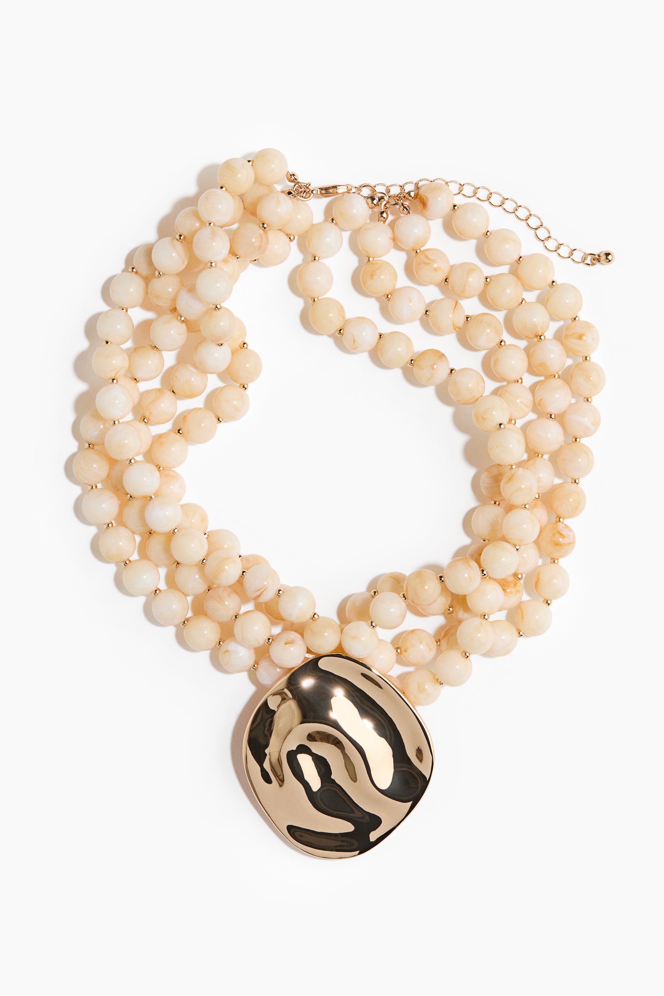 View larger image: This necklace showcases three strands of round, marbled cream beads, interspersed with small gold-tone spacers. At the centre hangs a large, glossy gold-tone pendant with a wavy, irregular surface. A gold-tone lobster clasp with an extender chain is visible at the top right.