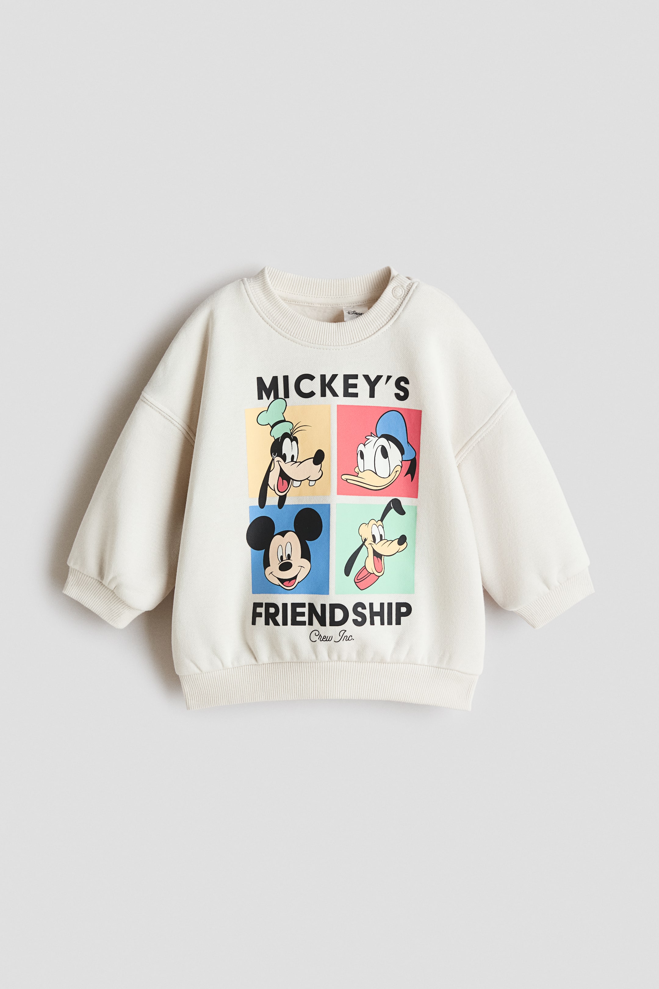 View larger image: A cream-colored printed sweatshirt is presenting its front, featuring a round neckline with two snap buttons on the right shoulder. The front is displaying a large graphic of four Disney characters in individual squares, with 'MICKEY'S FRIENDSHIP' and 'Crew Inc.' text below, and is also featuring ribbed cuffs and a ribbed hem.