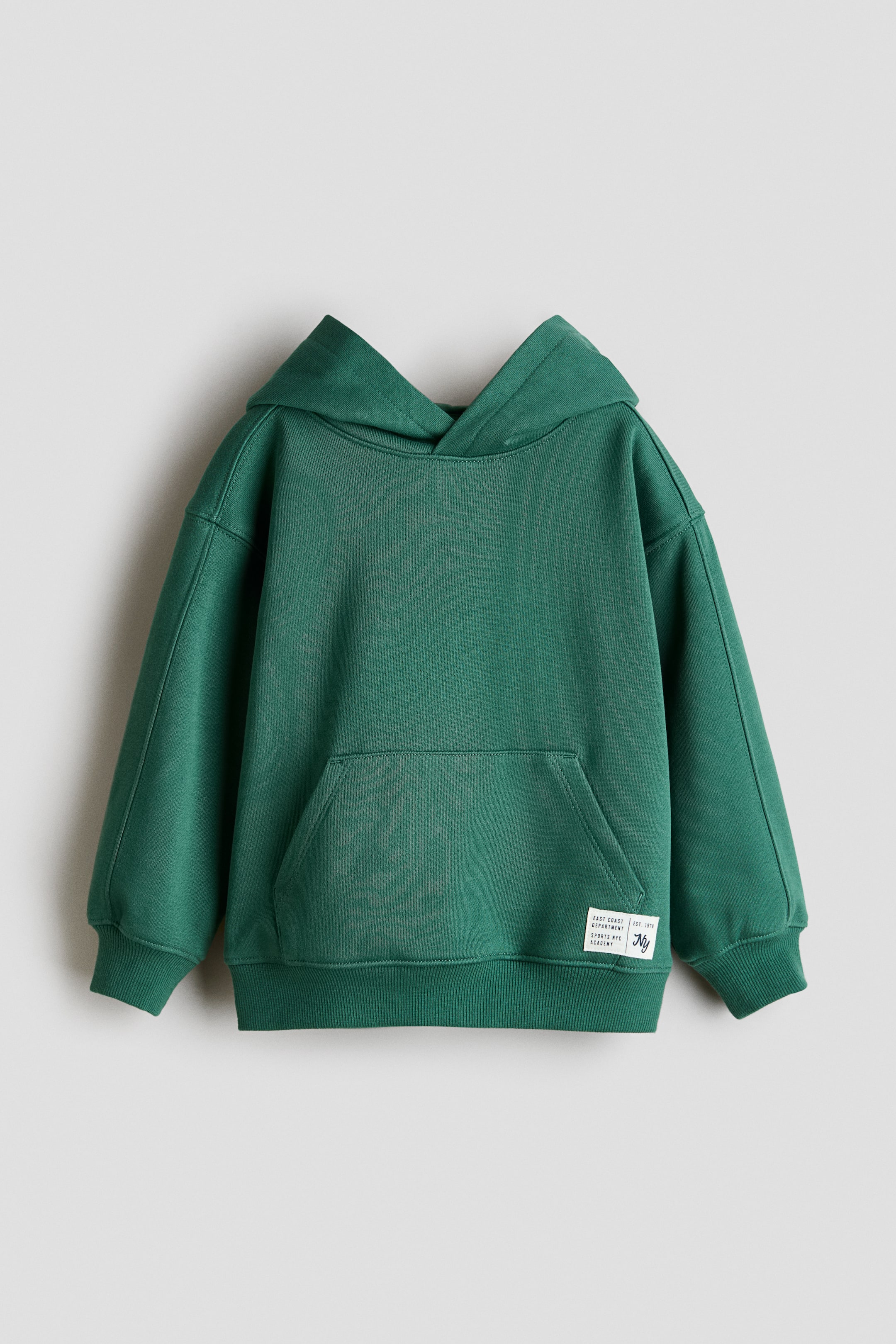 Größeres Bild anzeigen: Ein dunkelgrüner Hoodie ist von vorne zu sehen und verfügt über eine Kapuze, lange Ärmel mit Rippbündchen und einen gerippten Saum. Auf der Vorderseite befindet sich eine große Kängurutasche, und unten rechts vorne ist ein kleines weißes Stoffetikett mit schwarzer Schrift aufgenäht.