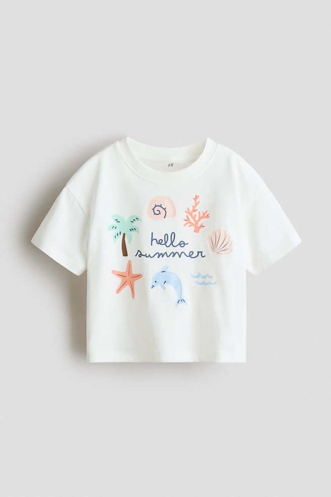 オフホワイトのコットンジャージーで作られたリラックスフィットのTシャツが前面に登場。ラウンドネックはリブトリムで仕上げられ、肩が落ちたデザインです。前面には、ヤシの木、ヒトデ、イルカ、巻貝、サンゴ、波を含むカラフルな「ハローサマー」プリントが施されています。 - 1