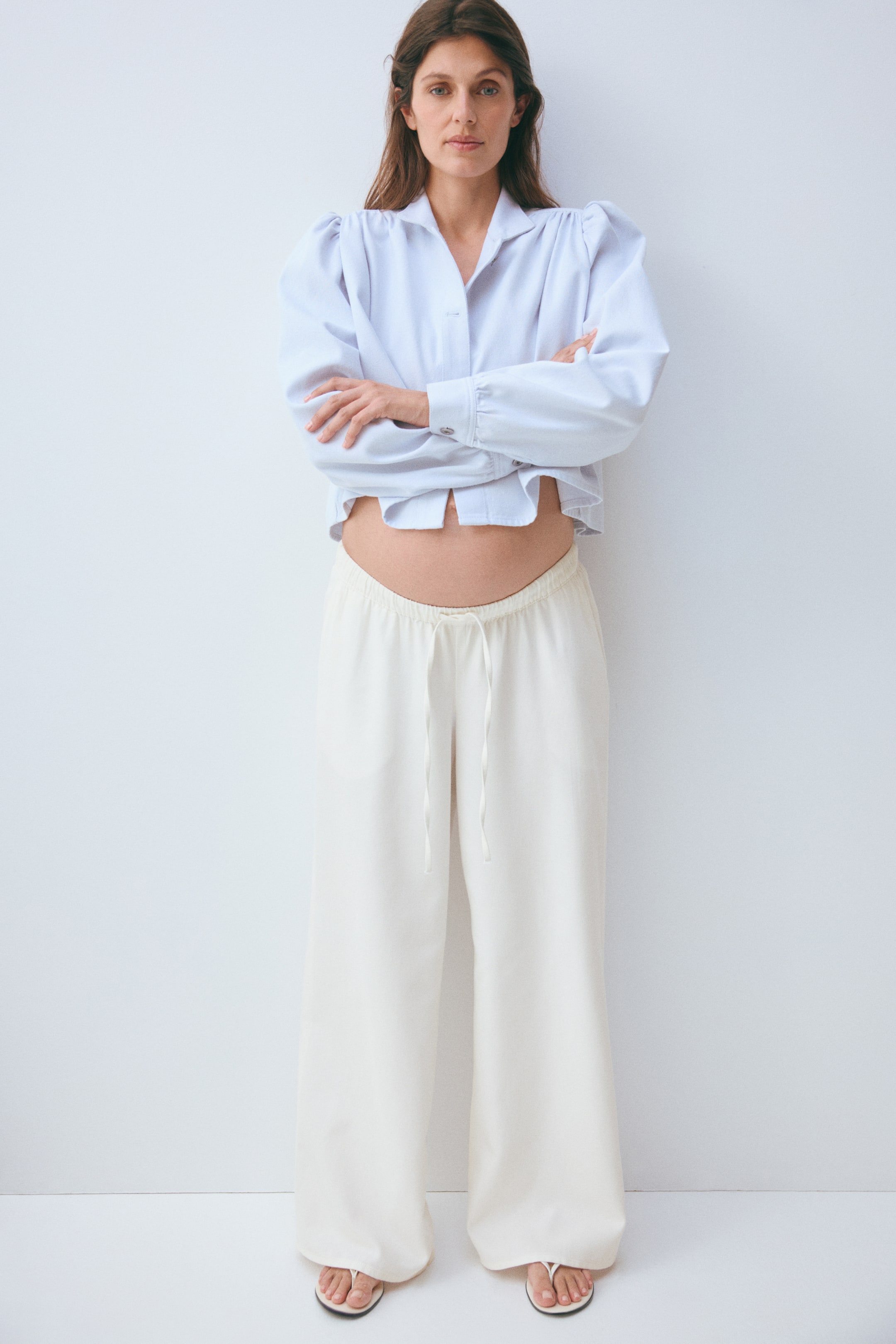 View larger image: Off-white wide-leg pants feature a drawstring waist and a full-length silhouette, slightly pooling at the feet.