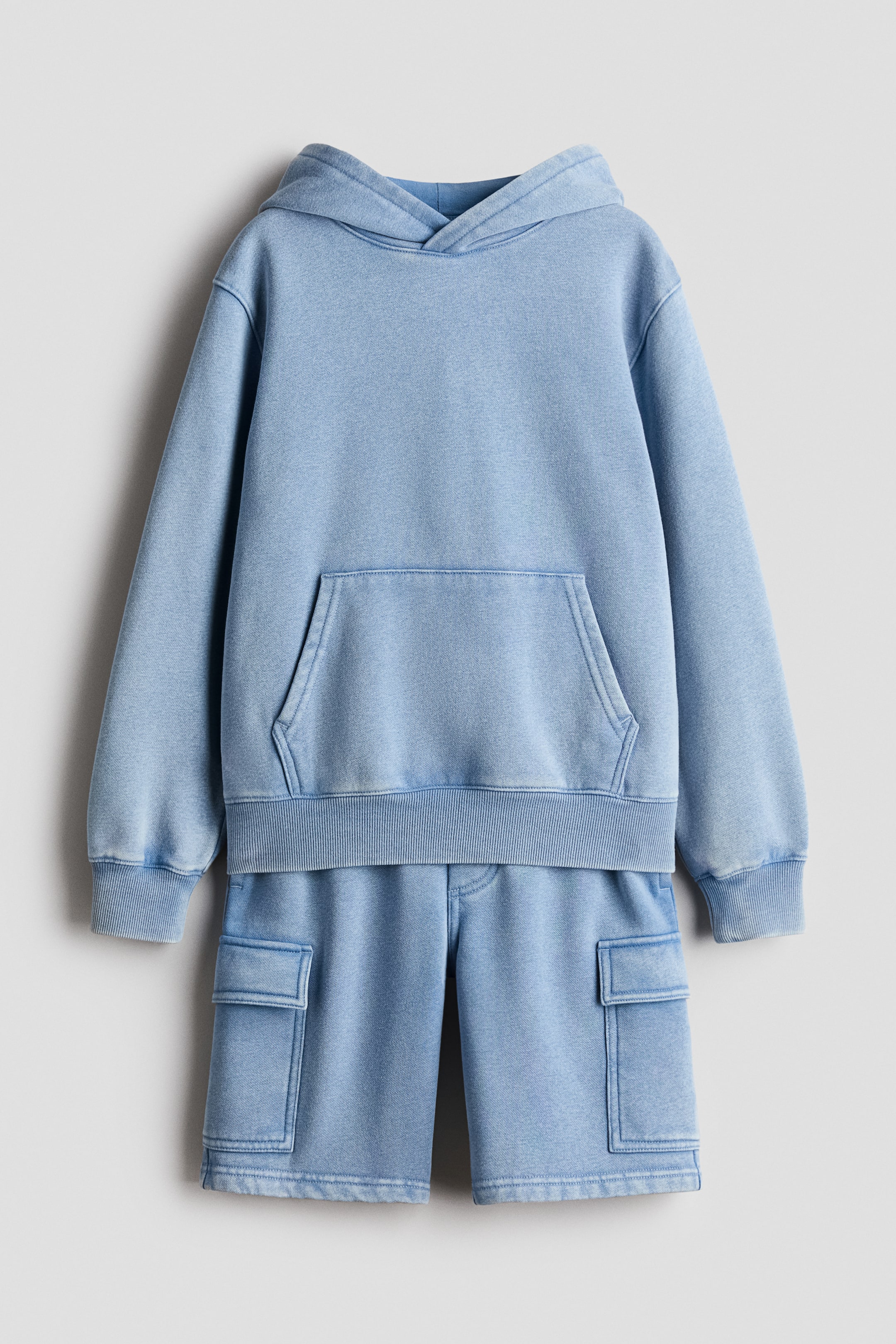 View larger image: A light blue washed-look two-piece set, consisting of a front-facing hoodie and shorts, is displayed. The hoodie features a hood, long sleeves with ribbed cuffs, a ribbed hem, and a kangaroo pocket, while the shorts showcase side cargo pockets.