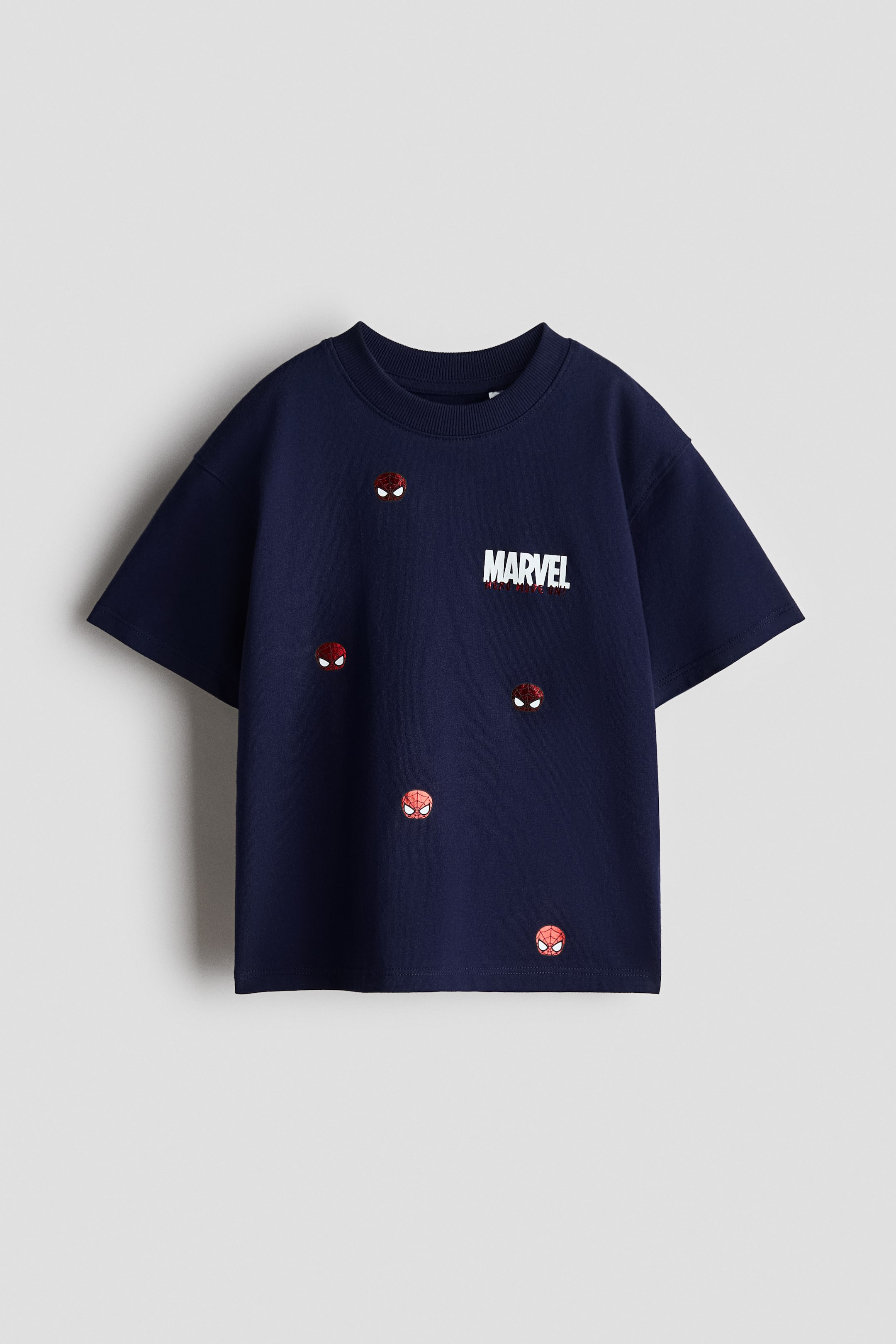 View larger image: An oversized T‑shirt in dark blue cotton jersey, featuring a white 'MARVEL' print with red accents and scattered small red-and-black Spider‑Man head motifs on the front. It has a round, rib‑trimmed neckline and dropped shoulders.