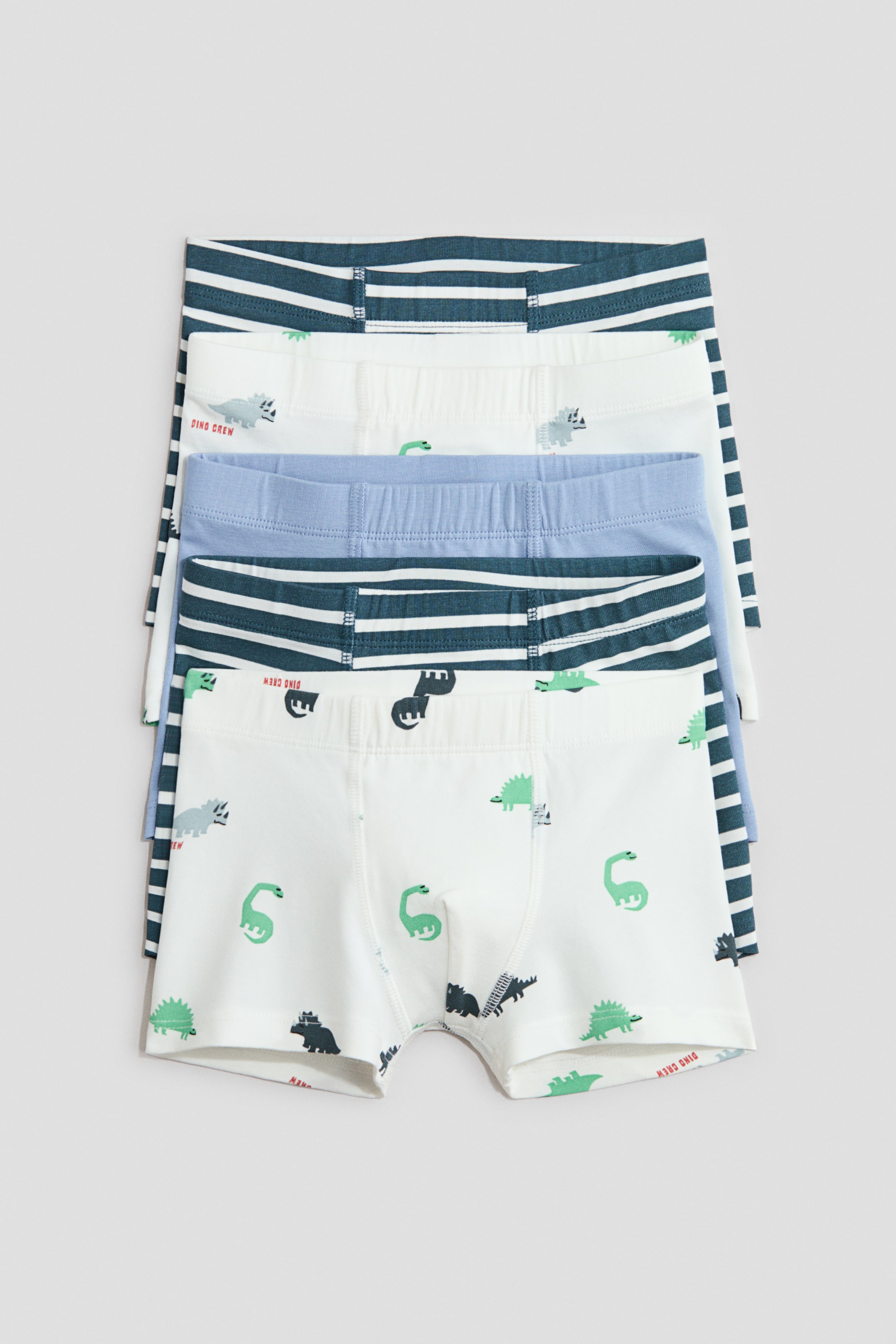 View larger image: A stack of four boys' boxer briefs is displayed from the front, with the top brief showcasing a white fabric adorned with green and grey dinosaur patterns and a blue elastic waistband. Below it, you can see a dark blue and white striped brief, a solid light blue brief, and another dark blue and white striped brief, each featuring an elastic waistband.