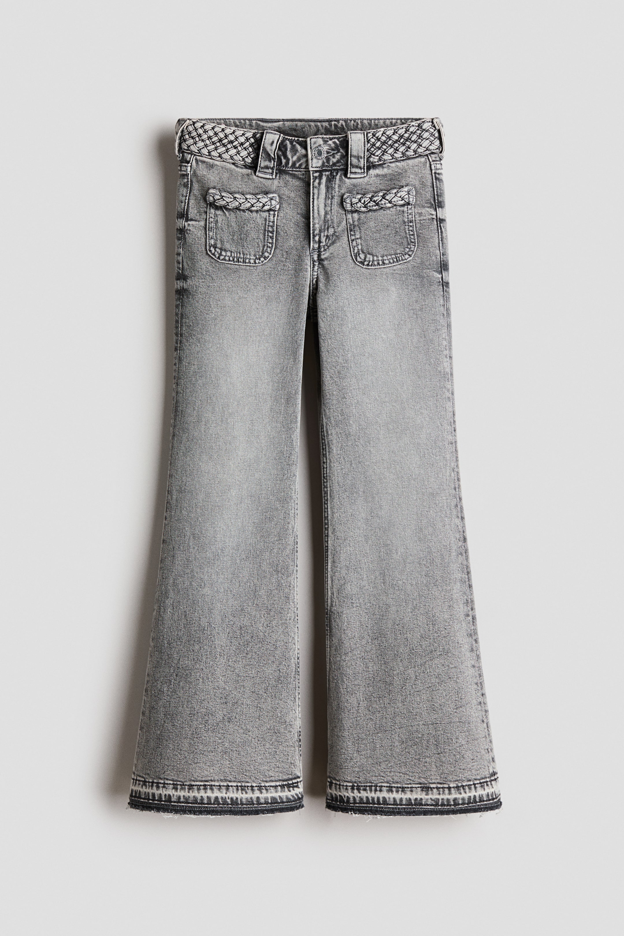 Größeres Bild anzeigen: Graue 5-Pocket-Jeans präsentieren sich vorne mit einer regulären Passform an Hüfte und Oberschenkel und ausgestellten Beinen. Sie verfügen über einen verstellbaren, elastischen Bund mit Reißverschluss und Knopf, ein gewebtes, gemustertes Band um die Taille, zwei vordere aufgesetzte Taschen mit geflochtenem Besatz und ausgefransten Säumen mit einem dekorativen, gemusterten Band.