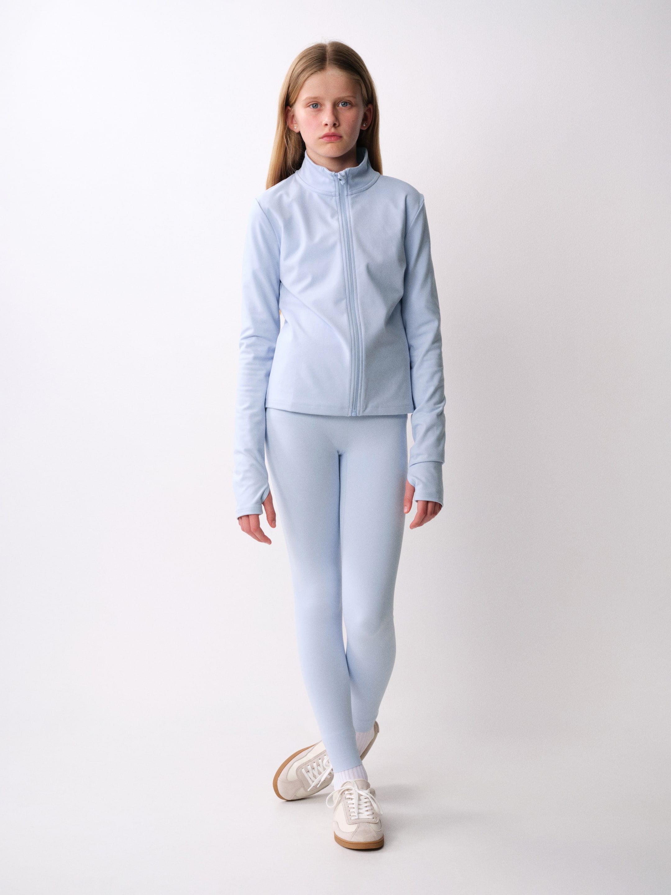 Visualizza l'immagine ingrandita: Un completo activewear azzurro chiaro viene mostrato frontalmente, composto da una giacca zip-up con collo alto finto e leggings aderenti coordinati. La giacca presenta una cerniera frontale a tutta lunghezza e maniche lunghe con polsini con foro per il pollice, mentre i leggings arrivano fino alle caviglie.