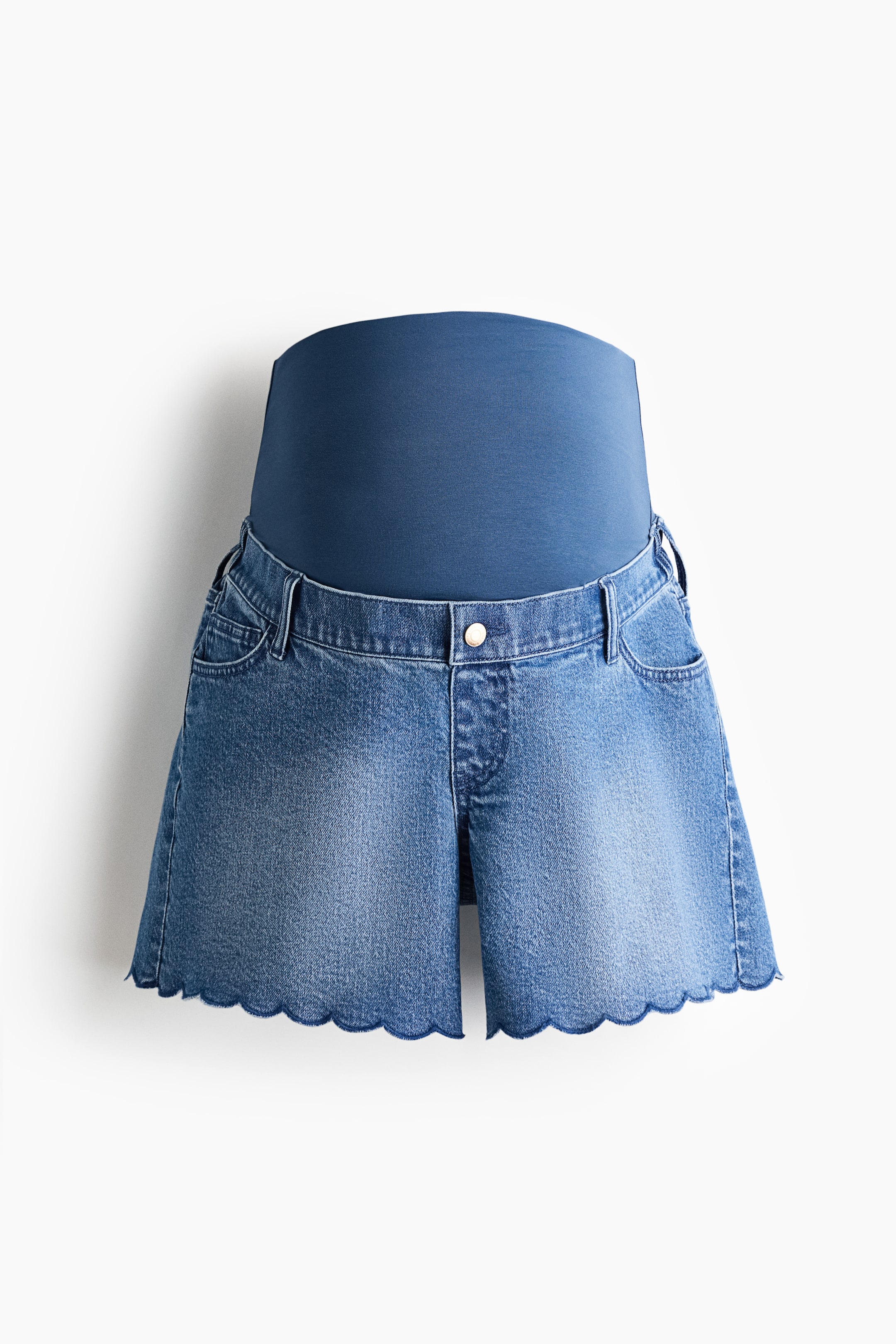 View larger image: Maternity denim shorts are shown from the front, featuring a wide, dark blue stretch fabric panel at the waist and light blue denim shorts. The shorts display a faded wash, belt loops, front pockets, a silver-toned button closure, and scalloped leg openings.