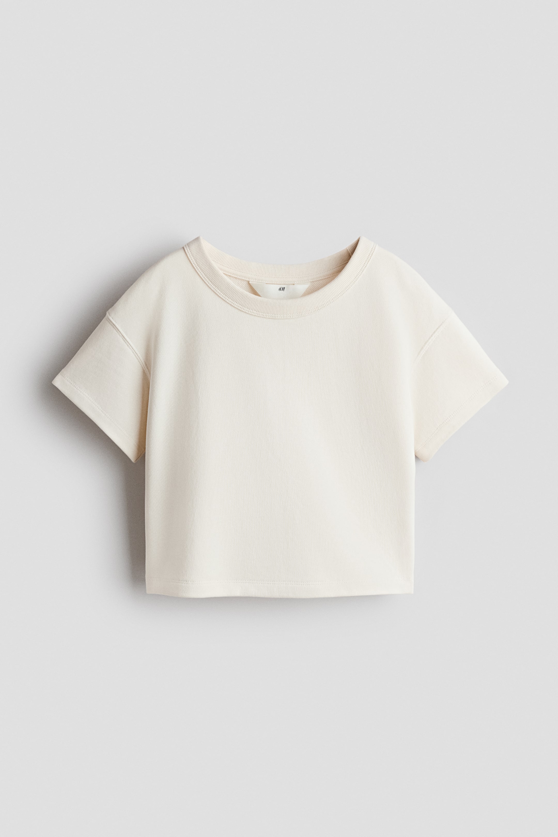 View larger image: A cream t-shirt is facing front, showcasing a ribbed crew neck and short sleeves. It features visible stitching along the shoulder seams and a straight hem.