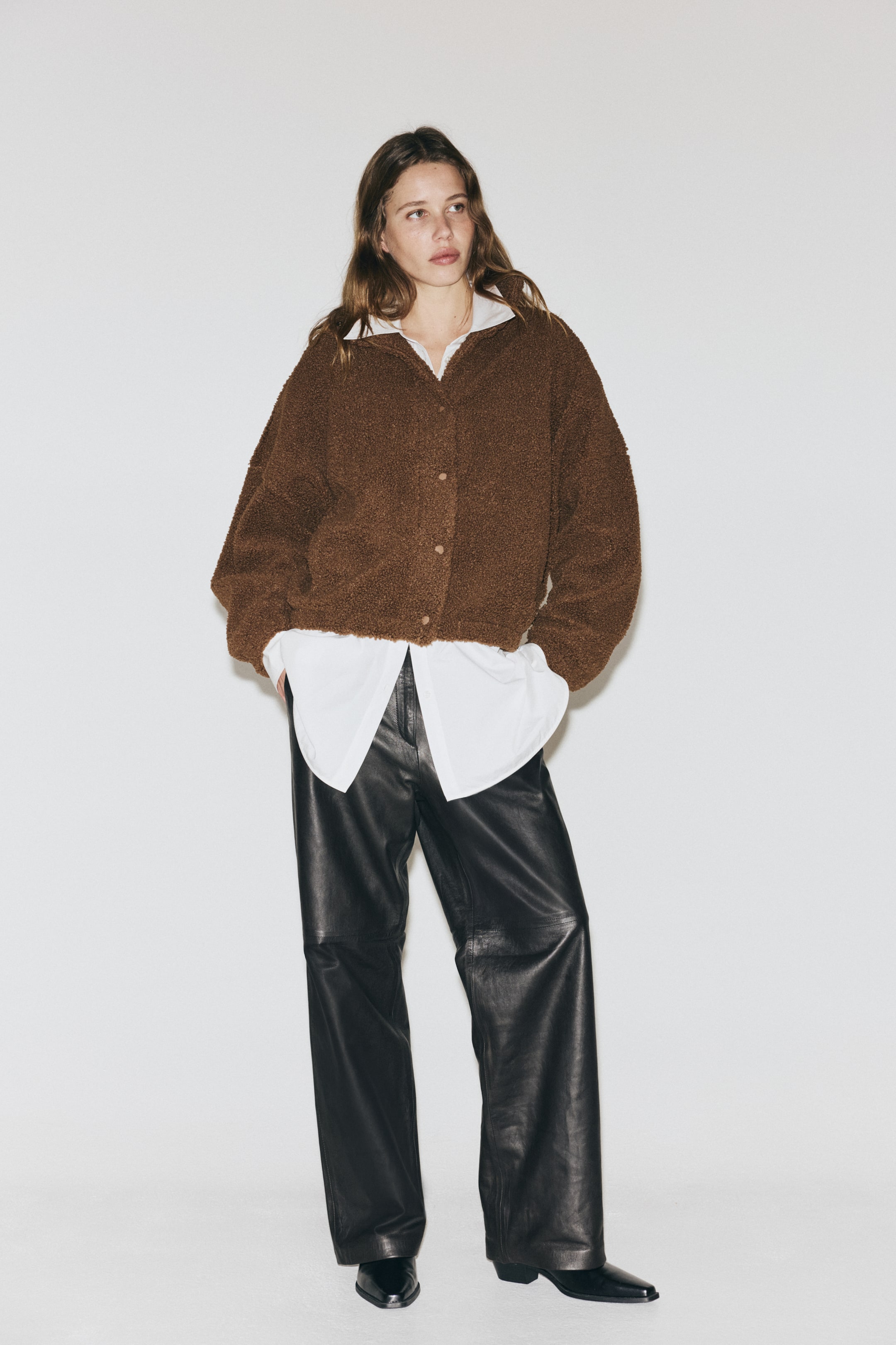 Visualizza immagine più grande: Una giacca teddy marrone è rivolta verso la parte anteriore, mostrando un materiale morbido e strutturato. Presenta un collo alto, una chiusura frontale con bottoni visibili, spalle scese e tasche a filetto laterali, ed è indossata aperta su una camicia bianca.