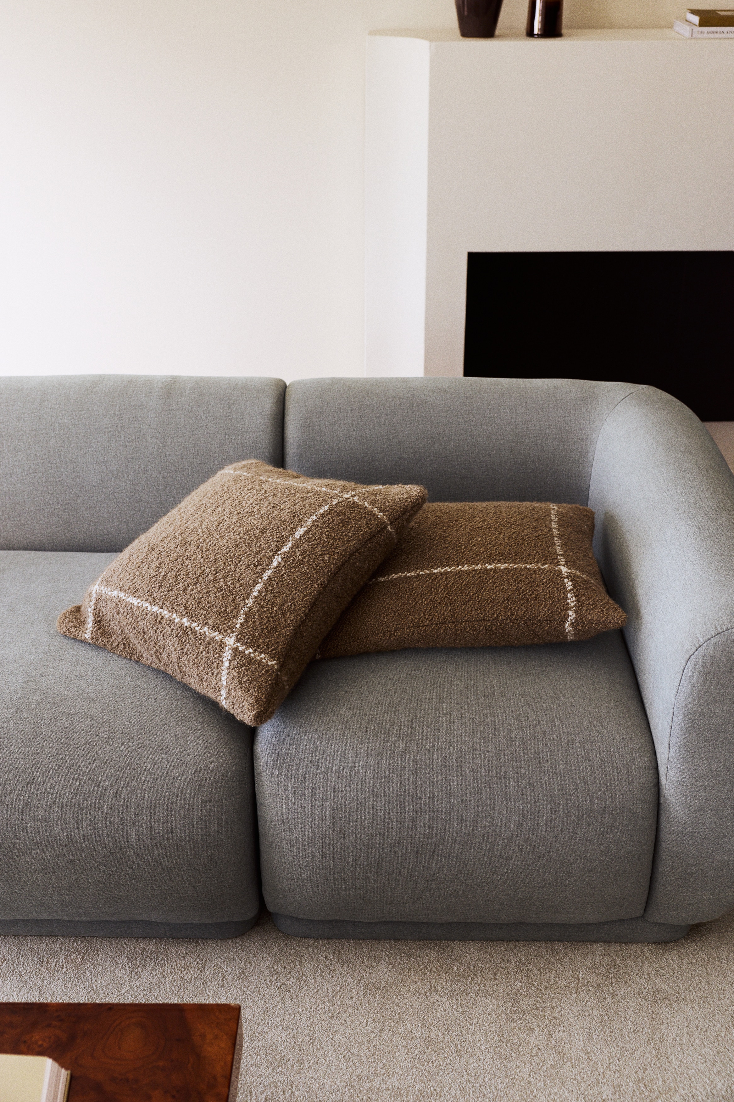 A square cushion is displaying a textured brown boucl� fabric, featuring an off-white grid pattern across its surface.