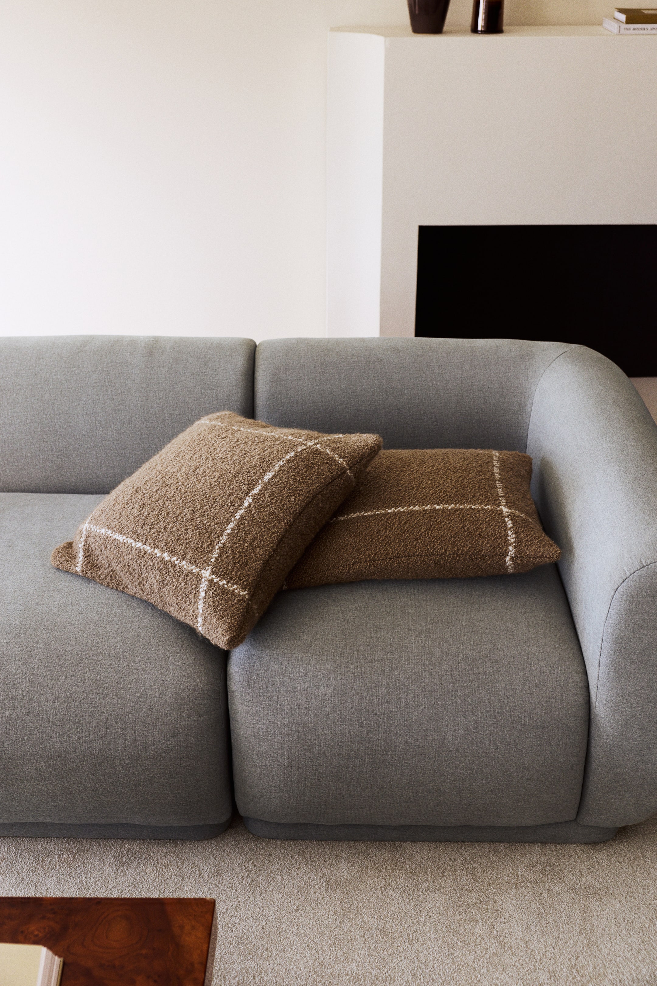 Agrandir l'image: Deux coussins déco marron présentant une texture bouclée et granuleuse ainsi qu’un motif à carreaux « windowpane » blanc reposent sur un canapé en tissu gris. Les coussins affichent un design moelleux et carré, se chevauchant l’un l’autre sur l’assise.