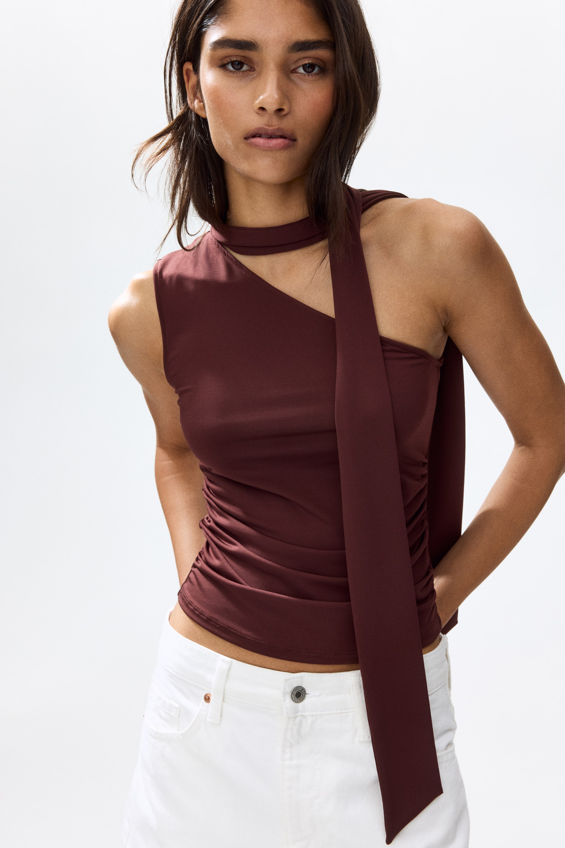 View larger image: The model is showcasing a deep maroon one-shoulder stretch jersey top. It highlights a broad shoulder strap, an asymmetric design, a scarf collar, and gathered side seams that create a draped effect.