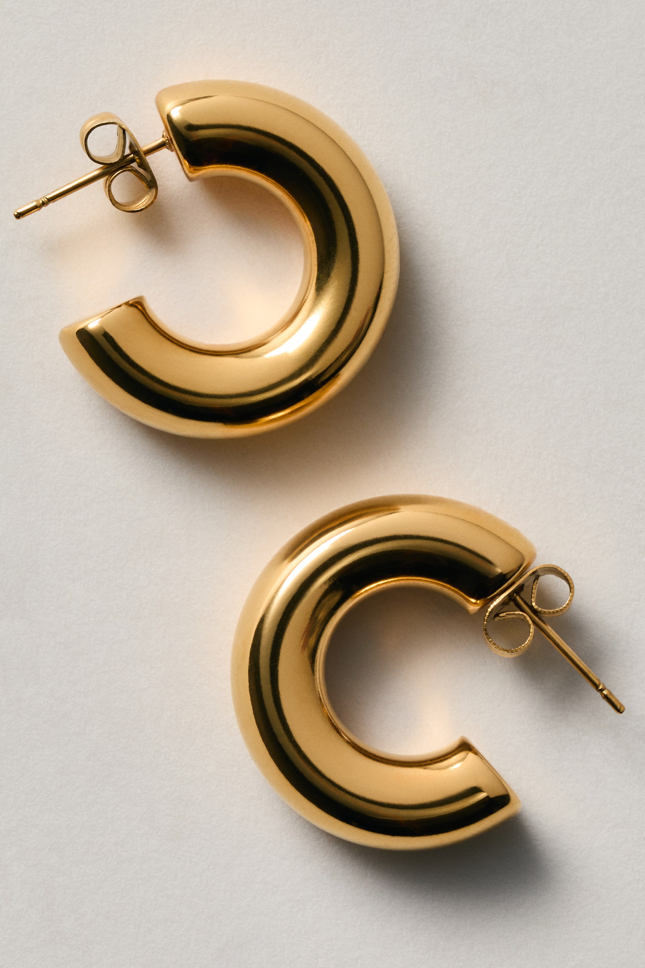 View larger image: Shiny gold-tone hoop earrings are designed as two chunky, C-shaped hoops. Each earring features a post-back closure with a butterfly backing, with the front of each hoop facing forward.