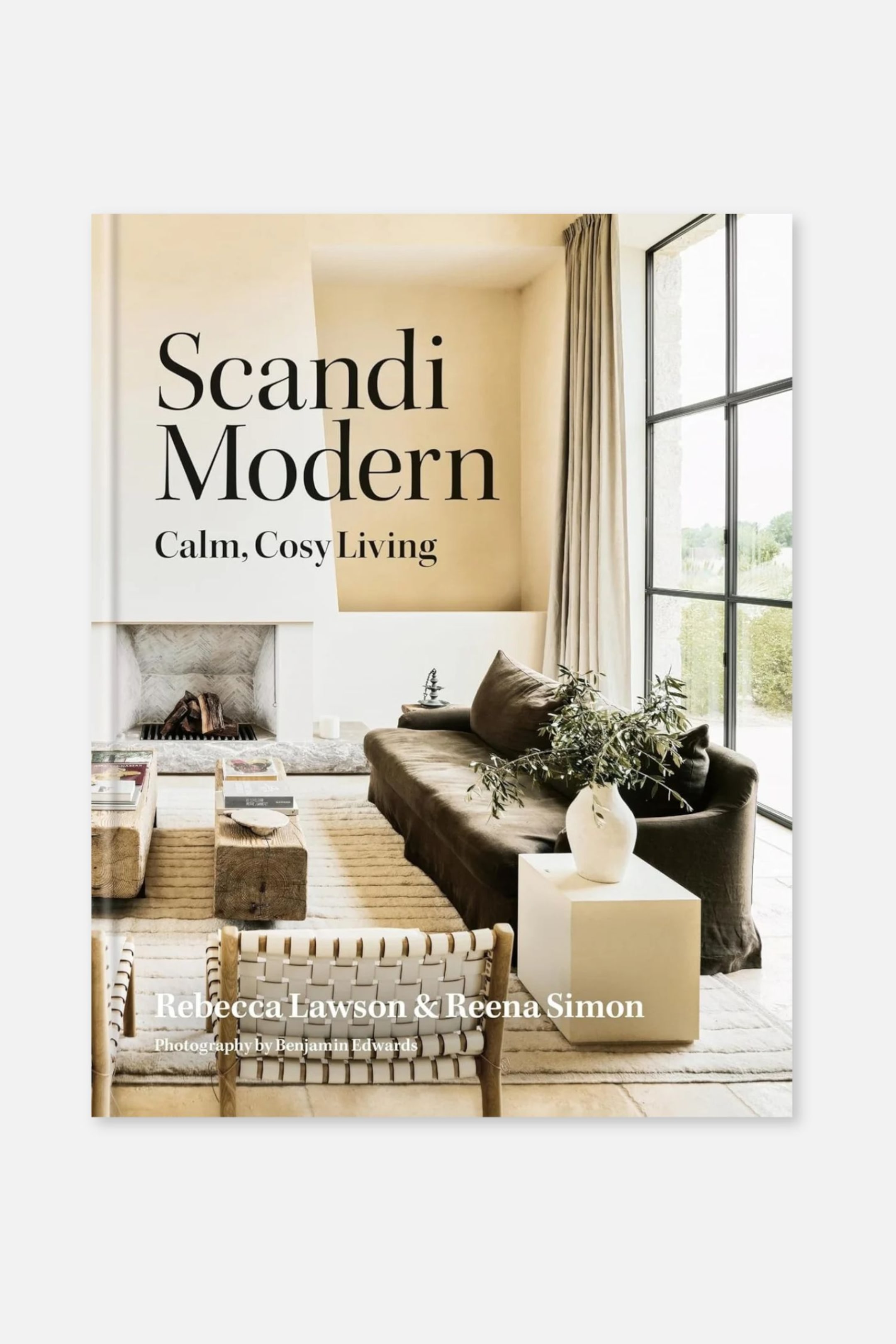 Zobacz większy obraz: Okładka książki „Scandi Modern: Calm, Cosy Living” przedstawia widok z przodu minimalistycznego salonu w stonowanej, neutralnej kolorystyce, z brązową sofą, drewnianymi stolikami pomocniczymi i plecionym fotelem. Tytuł jest umieszczony u góry dużą czarną szeryfową czcionką, a nazwiska autorek, Rebecca Lawson i Reena Simon, zostały wydrukowane białym tekstem na dole.