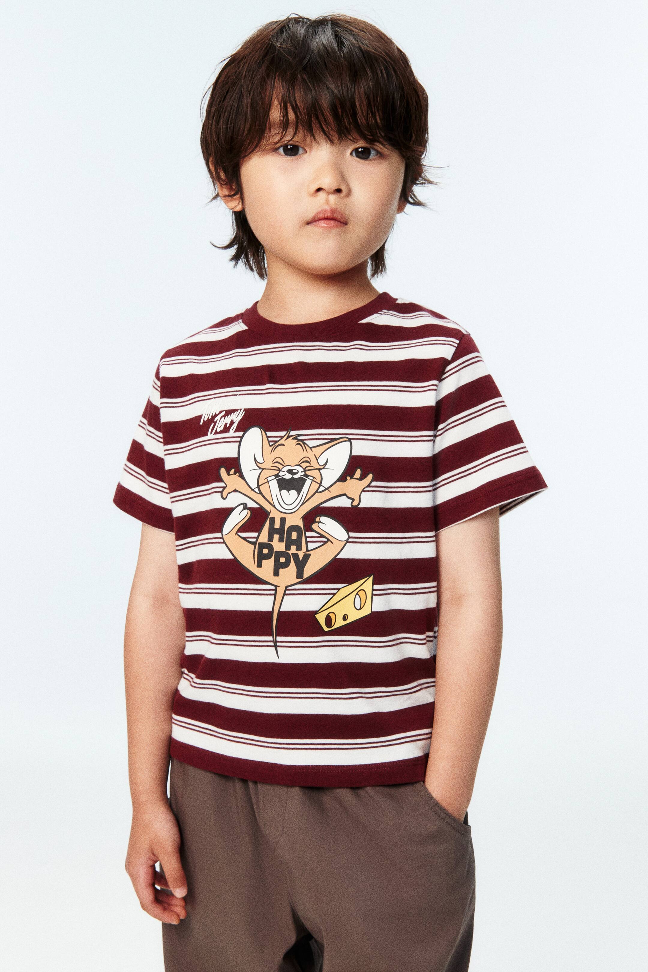 View larger image: Ang modelo ay nakasuot ng T-shirt na gawa sa malambot na cotton jersey. Ito ay may mga pahalang na guhit na kulay burgundy at puti, may print na motibo ng cartoon mouse na may "HAPPY" na teksto sa harap, at bilog na neckline na may rib trim.