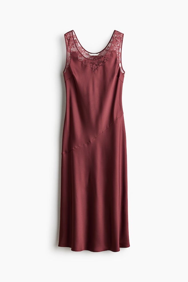 The burgundy slip dress showcases a scoop neckline adorned with intricate lace detailing across the upper chest, seamlessly forming the shoulder straps. Crafted from lustrous fabric, the dress features a diagonal seam that elegantly traverses the front, extending to a sophisticated midi length. - 1