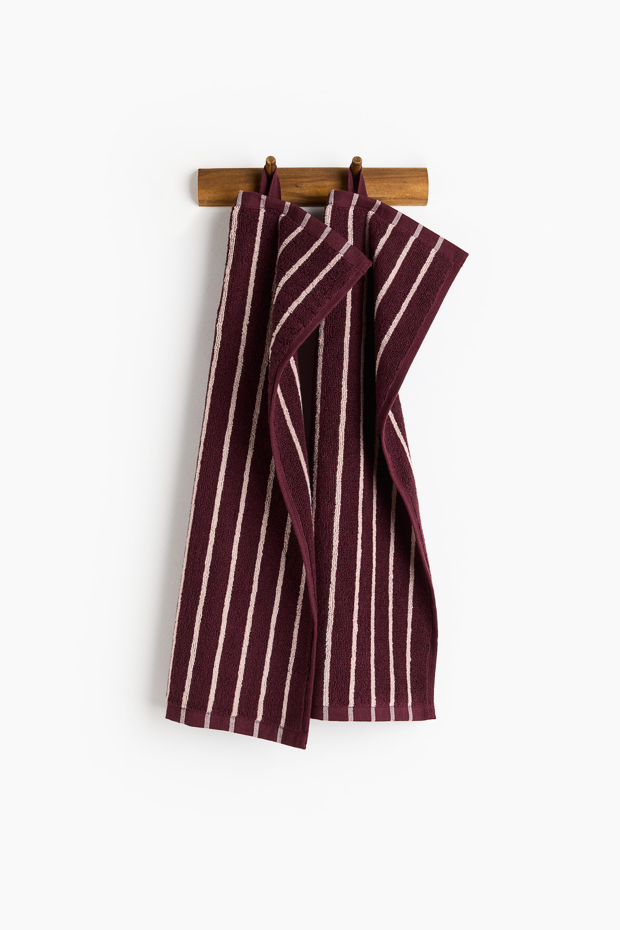 View larger image: Two burgundy towels, featuring light beige vertical stripes, are hanging vertically from a wooden rack. The towels are slightly overlapping.