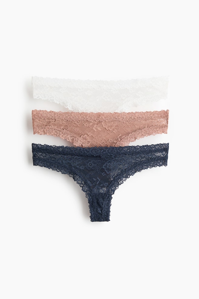 Tres braguitas brasileñas presentan su parte frontal, confeccionadas en encaje con cintura baja. Cuentan con un refuerzo forrado y un diseño de corte alto, disponibles en blanco, rosa empolvado y azul oscuro. - 1