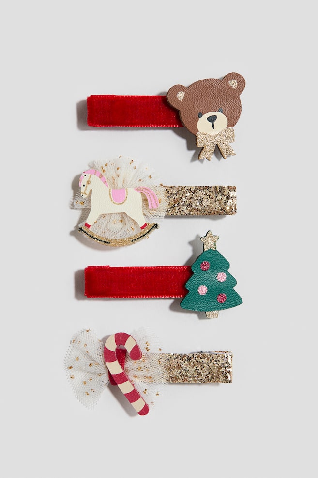 A four-pack of hair clips is presenting from the front, arranged vertically to showcase distinct decorative designs. The first and third clips are featuring red velvet-wrapped bases adorned with a brown bear wearing a gold glitter bow and a green tree with pink ornaments and a gold star, respectively. The second and fourth clips are displaying gold glitter-covered bases embellished with a white rocking horse on a white tulle puff and a red-and-cream striped candy cane on a white tulle bow. - 1